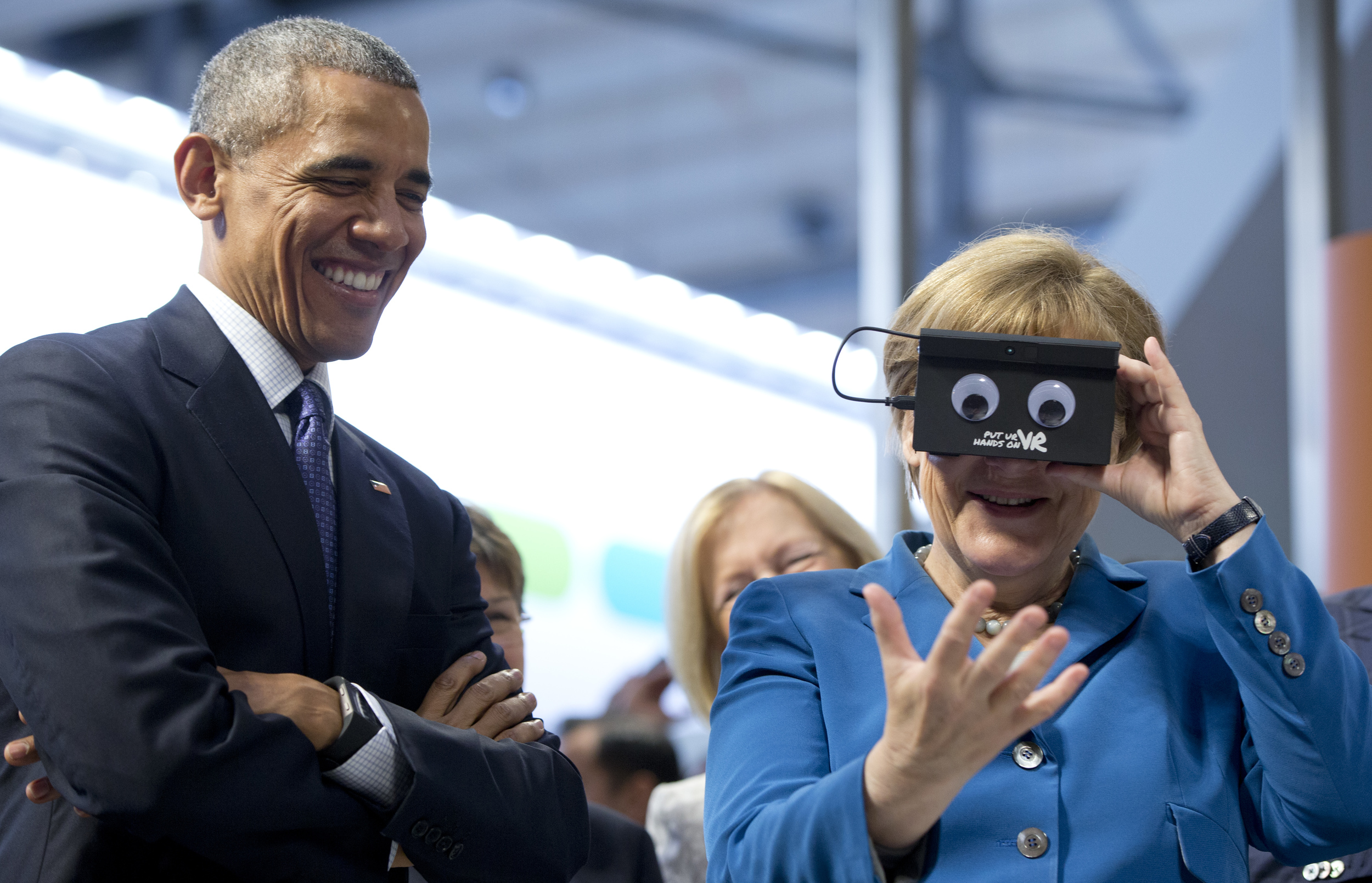 U.S. President Barack Obama looks on as German Chancellor Angela Merkel tests VR goggles when touring the Hannover Messe, the world's largest industrial technology trade fair, in Hannover, northern Germany, Monday, April 25, 2016. Obama is on a two-day official visit to Germany. (AP Photo/Carolyn Kaster)