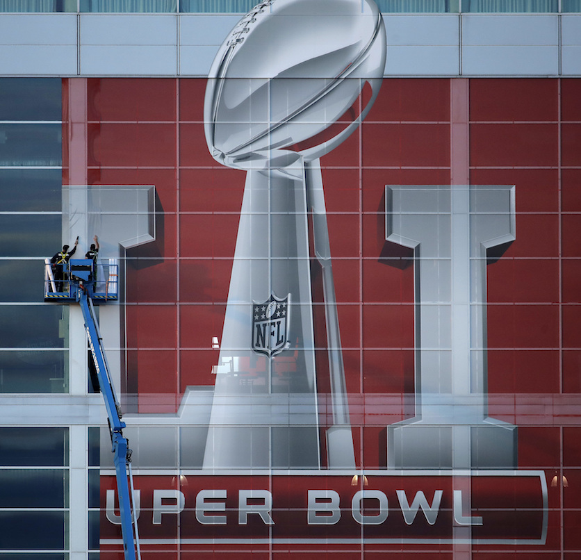Workers attach a sign to the front of NRG Stadium as preparations continue for the NFL Super Bowl 51 football game Sunday, Jan. 29, 2017, in Houston. (AP Photo/Charlie Riedel)