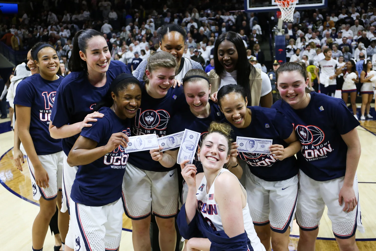The team poses with Geno Auriemma’s hundred-win dollar bills postgame. (Jackson Haigis/The Daily Campus)