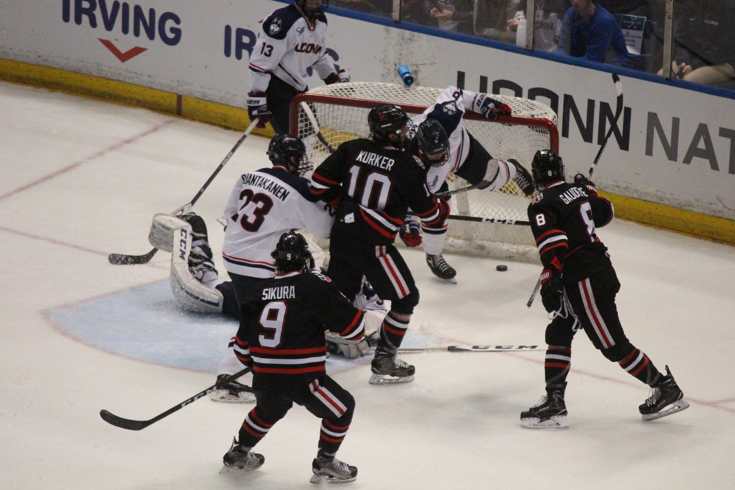 Northeastern's Dylan Sakura (#9), Sam Kurker (#10), and Adam Gaudette (#8) celebrate a goal. UConn forward Kasperi Ojantakanen (#23) looks on from the crease as goalie Adam Huska's (#30) diving effort wasn't enough. (Mustafe Mussa/The Daily Campus)