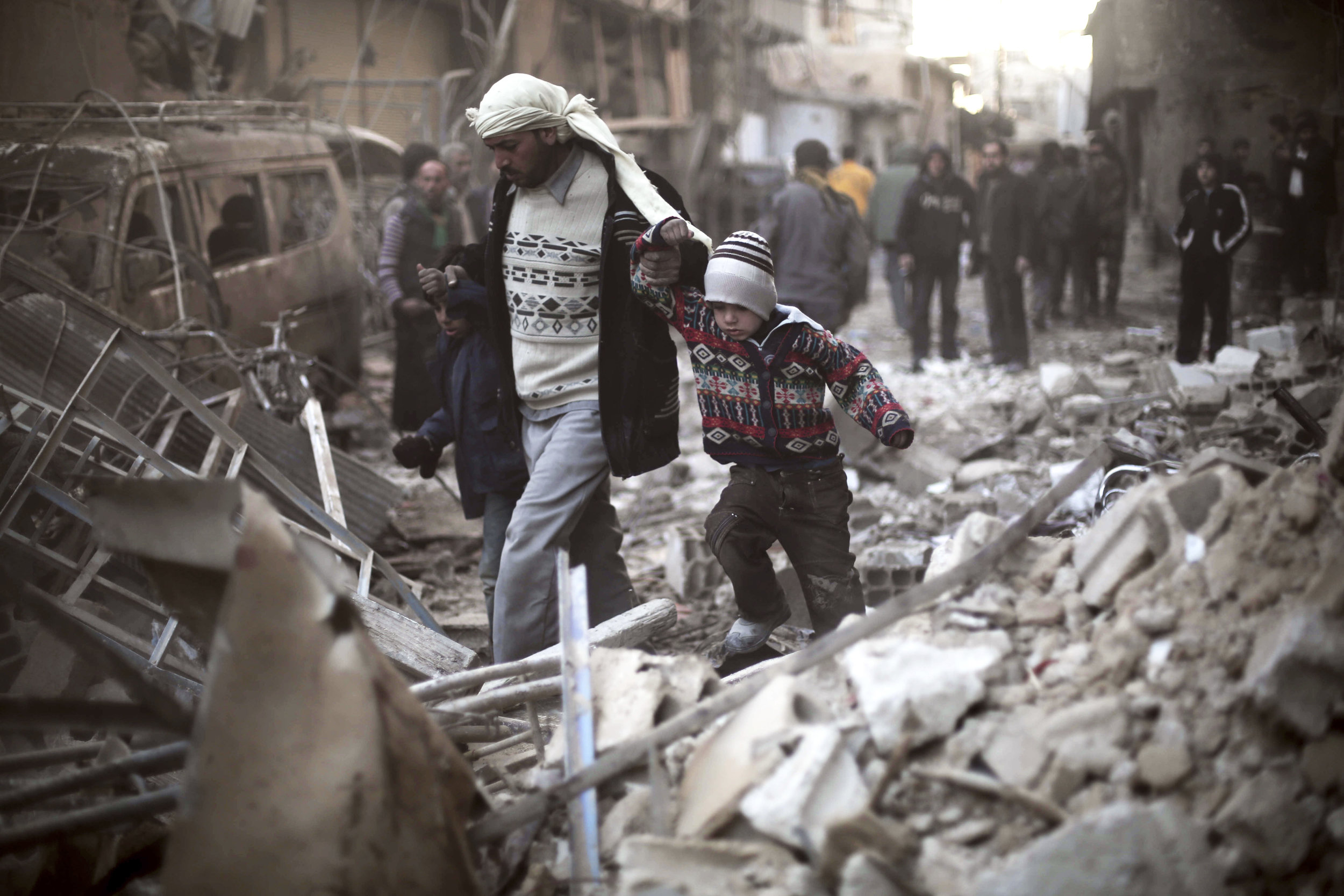 This Dec. 24, 2015 file photo provided by Save the Children, a man walks with a pair of children in hand hand through the rubble in Eastern Ghouta, Syria. (Save the Children via AP, File)