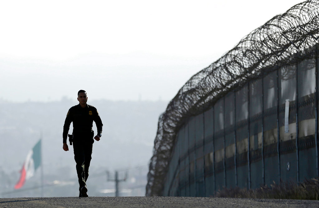 In this June 22, 2016 file photo, Border Patrol agent Eduardo Olmos walks near the secondary fence separating Tijuana, Mexico, background, and San Diego in San Diego. (AP Photo/Gregory Bull, File)