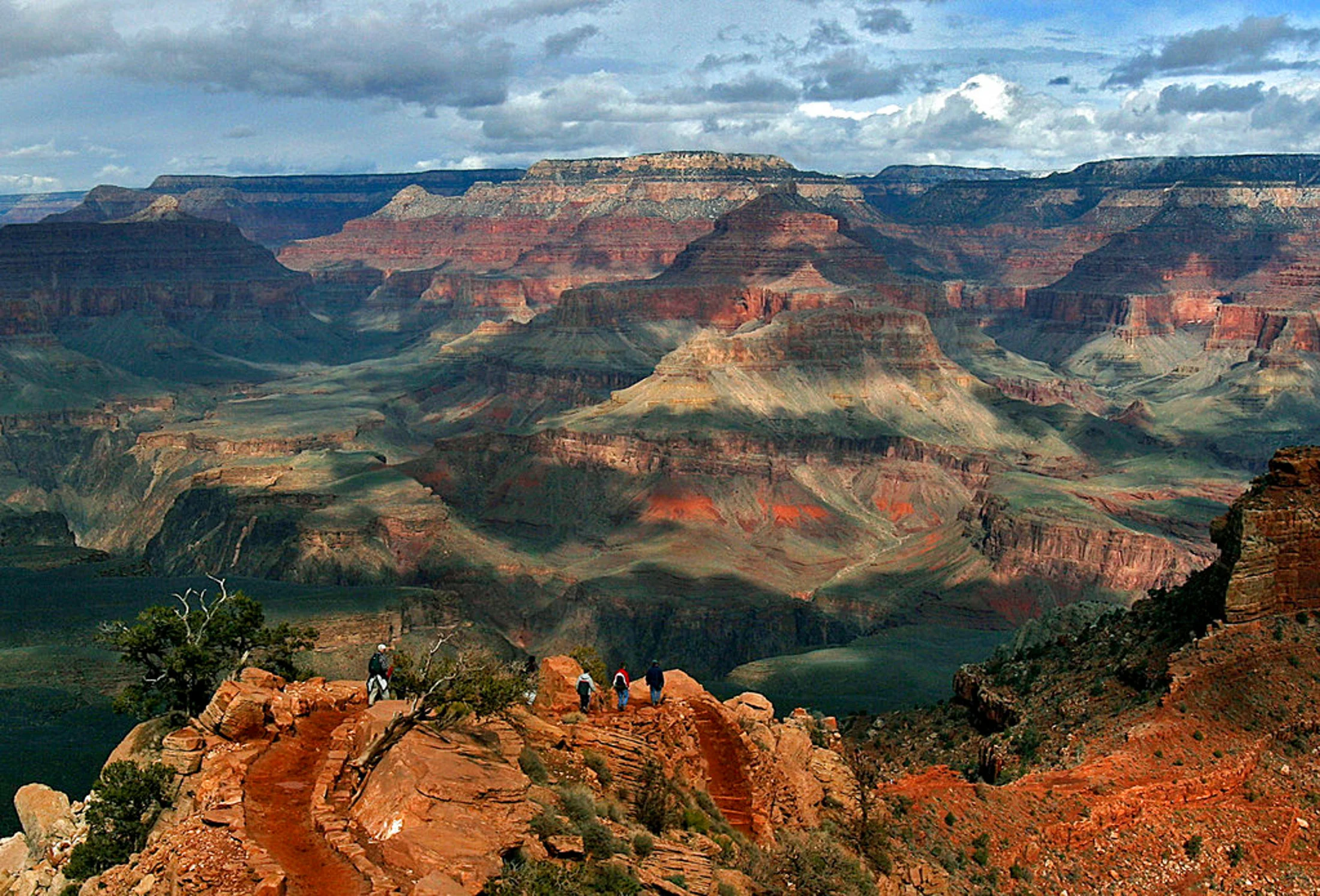 This Feb. 22, 2005 file photo shows the North Rim of the Grand Canyon, background, as tourists hike along the South Rim in Grand Canyon, Ariz. Lower snowfall in recent years at the Grand Canyon’s North Rim is prompting tourism officials to expand the visiting season for tourists. The North Rim typically closes from mid-October to mid-May because of snow. But the one road that goes into the lesser visited part of the Grand Canyon now often doesn’t have snow by Dec. 1. Tourism officials say climate change could work in their favor to bring in more visitors and revenue to the region. (AP Photo/Rick Hossman, File)