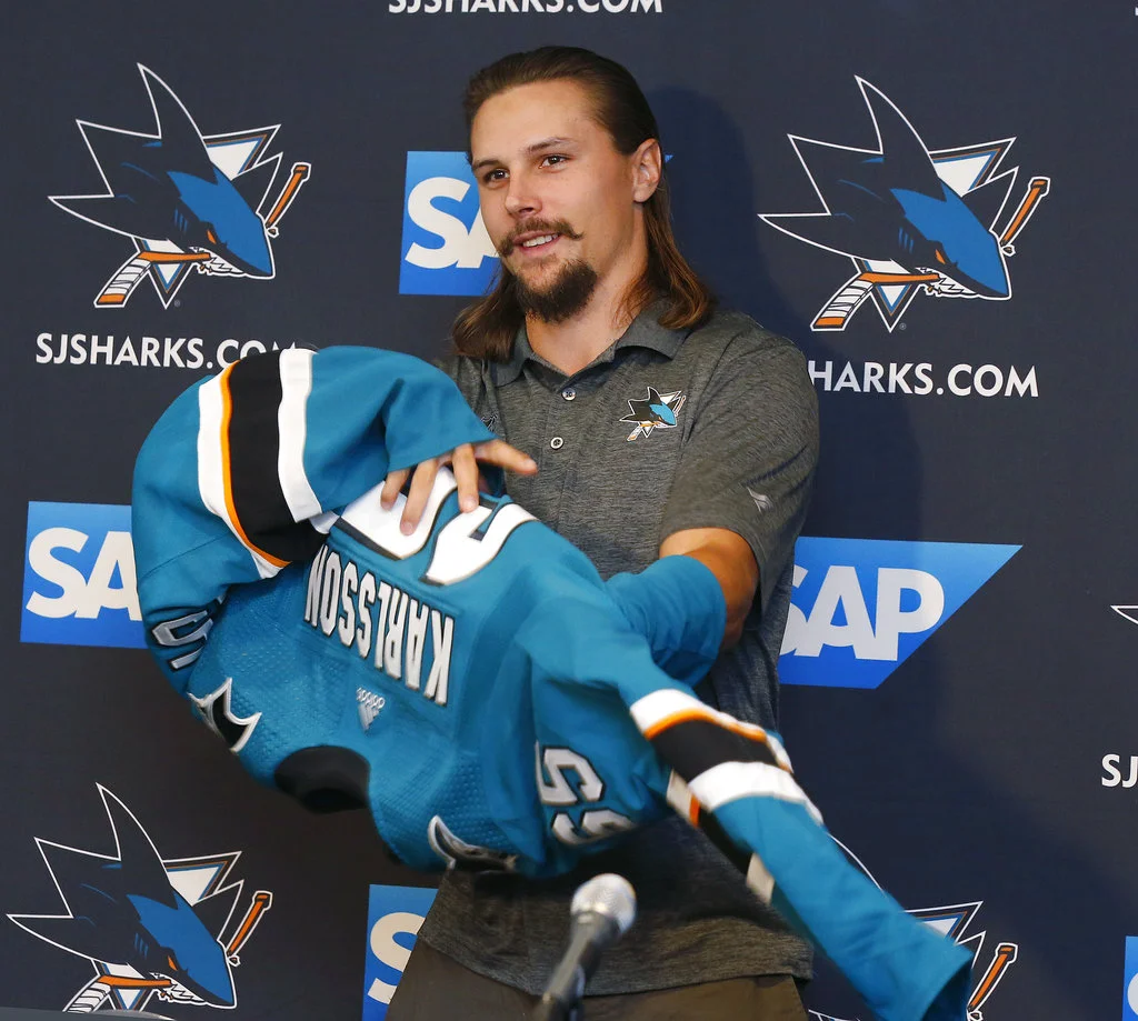 Newly acquired San Jose Sharks defenseman Erik Karlsson puts on jersey during a news conference held by the NHL hockey team in San Jose, Calif., Wednesday, Sept. 19, 2018. (AP Photo/Josie Lepe)