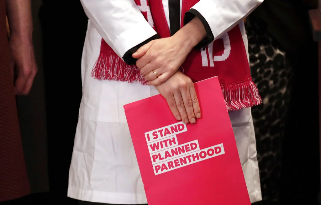 Dr. Erin Berry, Washington State Medical Director for Planned Parenthood of the Great Northwest and the Hawaiian Islands, holds a folder as she listens at a news conference announcing a lawsuit challenging the Trump administration's Title X "gag rule" Monday, Feb. 25, 2019, in Seattle. The rule issued last Friday would impact federal funding for reproductive health care and family planning services. (AP Photo/Elaine Thompson)