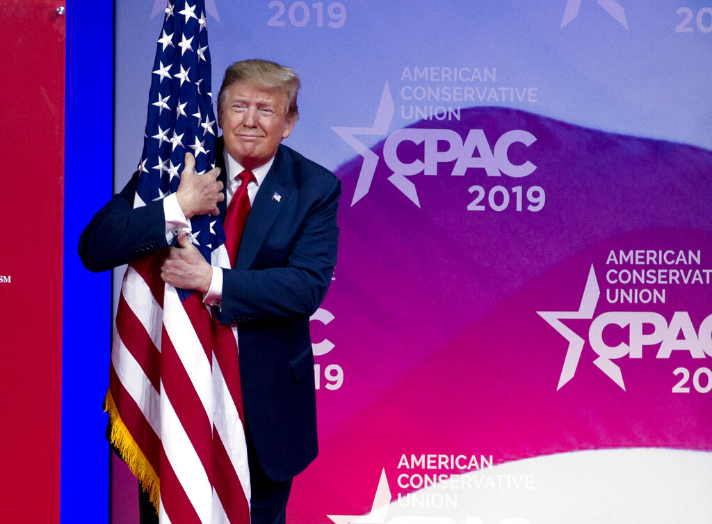 President Donald Trump hugs the American flag as he arrives to speak at Conservative Political Action Conference, CPAC 2019, in Oxon Hill, Md., Saturday, March 2, 2019. (AP Photo/Jose Luis Magana)