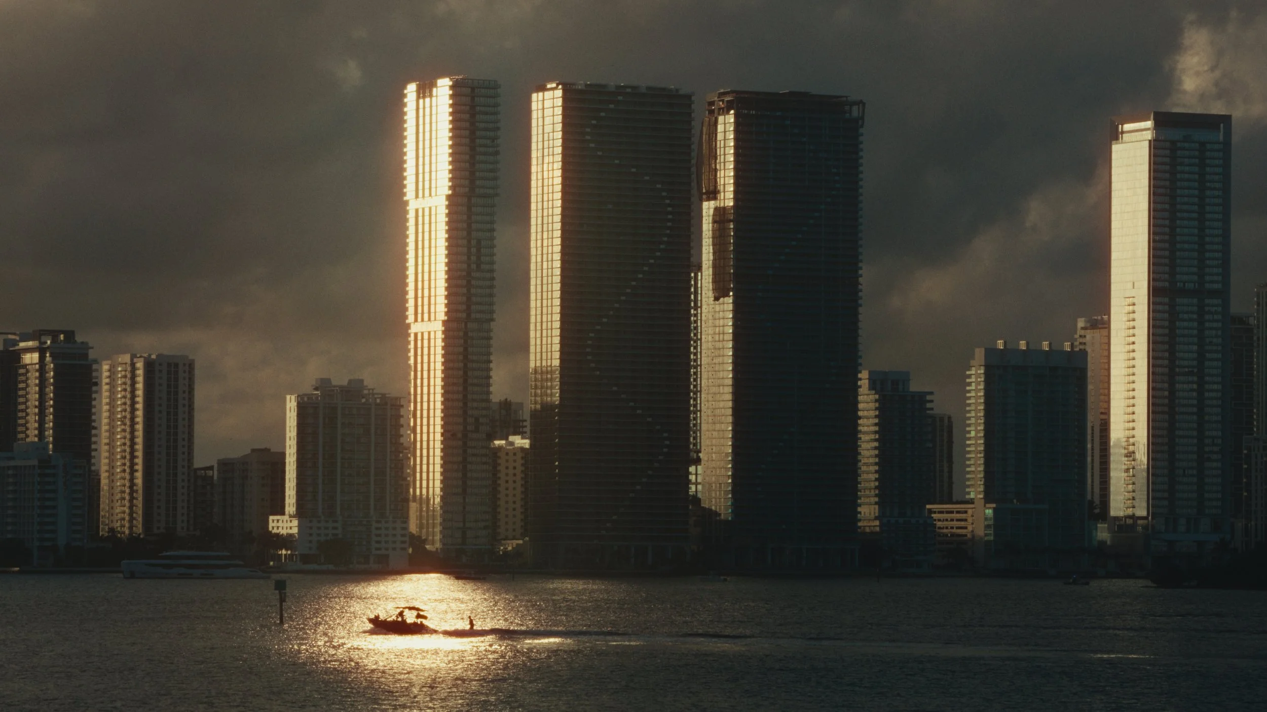Architectural photograph of the Sunny Isles Beach skyline glowing at golden hour across Biscayne Bay with a boat silhouetted on the water. Captured by Miami and Los Angeles-based architectural and travel photographer Christian Santiago