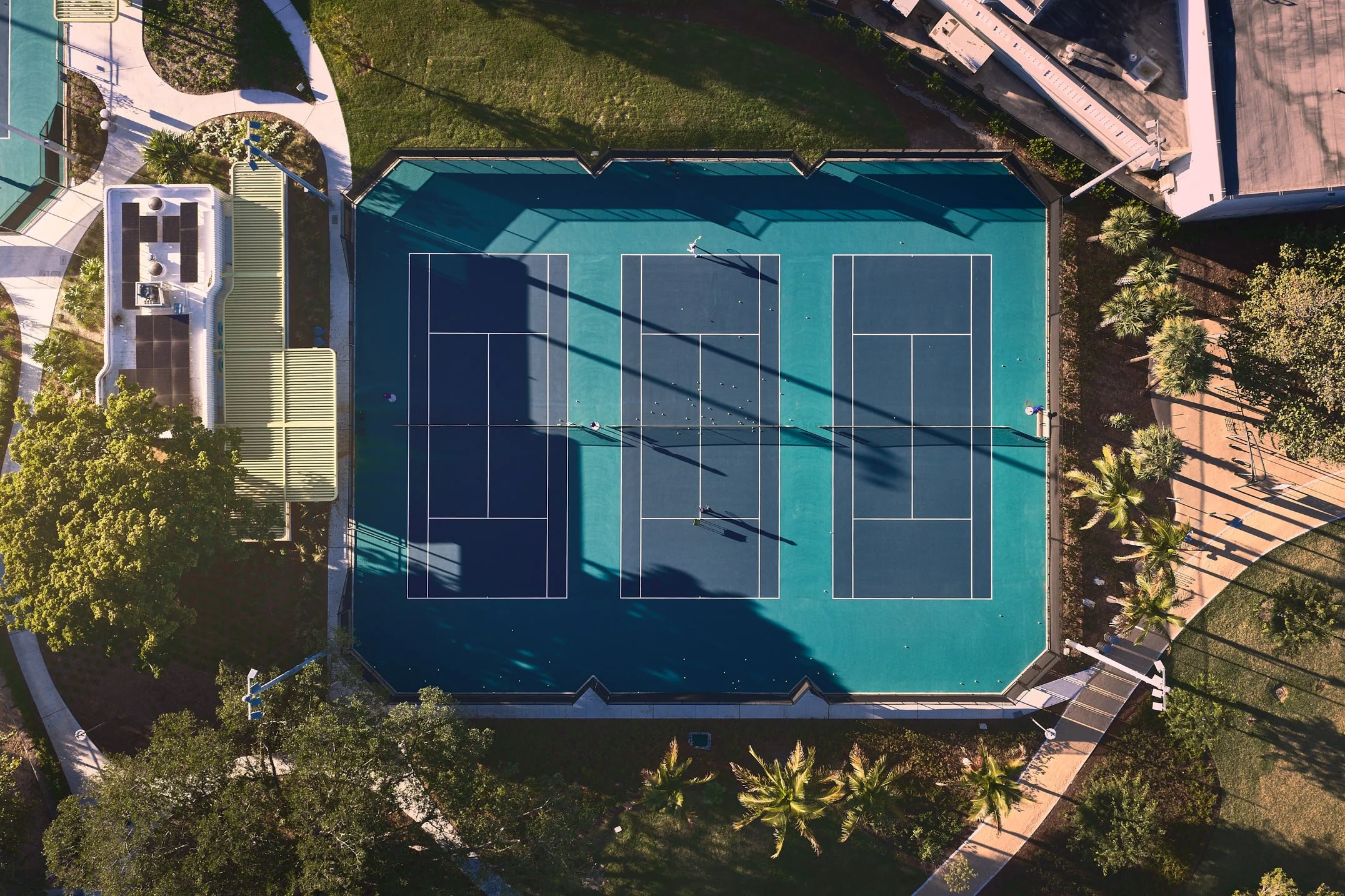 Architectural aerial photograph of tennis courts within Bayshore Park in Miami Beach, surrounded by landscaped pathways and palm trees that integrate recreational facilities into the park’s larger urban design. Captured by Miami and Los Angeles-based