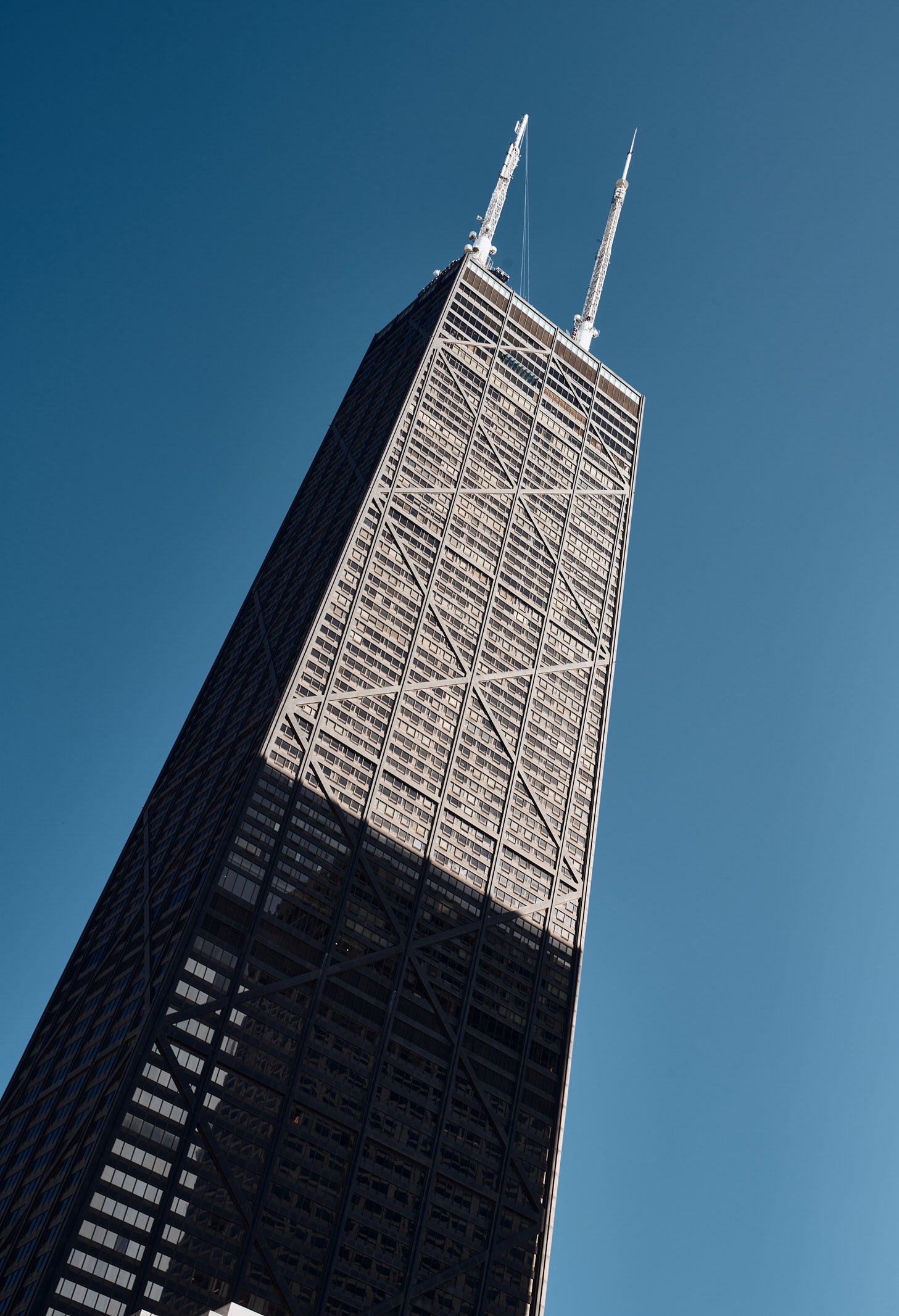 Architectural photograph of the John Hancock Center in Chicago, showcasing the iconic X-braced skyscraper rising behind Water Tower Place on a crisp, clear day. The historic Chicago Water Tower stands nearby, anchoring the image with a blend of moder