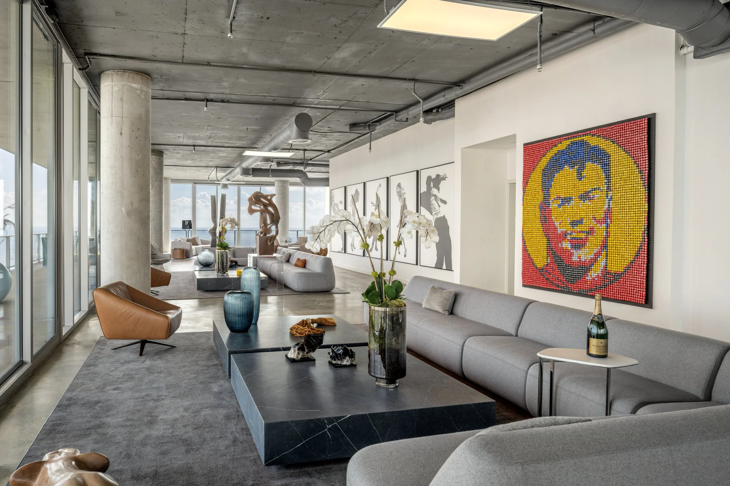 Architectural photograph of a luxury penthouse interior at the Grove at Grand Bay By Bjark Ingels featuring modern concrete ceilings, floor-to-ceiling windows with ocean views, and curated contemporary art including a vibrant portrait and large scul