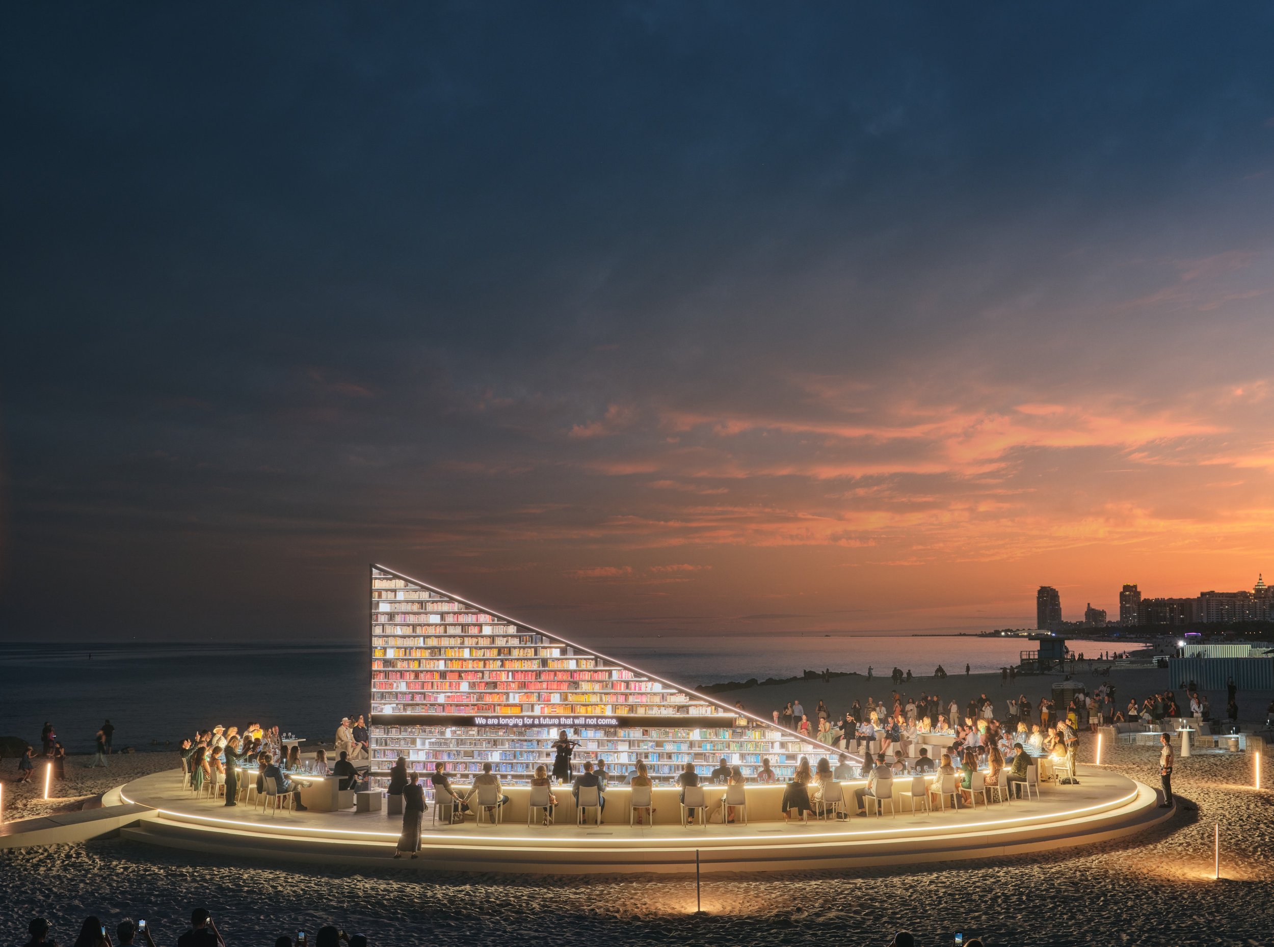 Architectural photograph of Es Devlin’s Library of Us public art installation at Faena Miami Beach during Art Basel, featuring a glowing triangular bookshelf structure surrounded by seated guests and visitors at sunset, with warm lighting contrasting