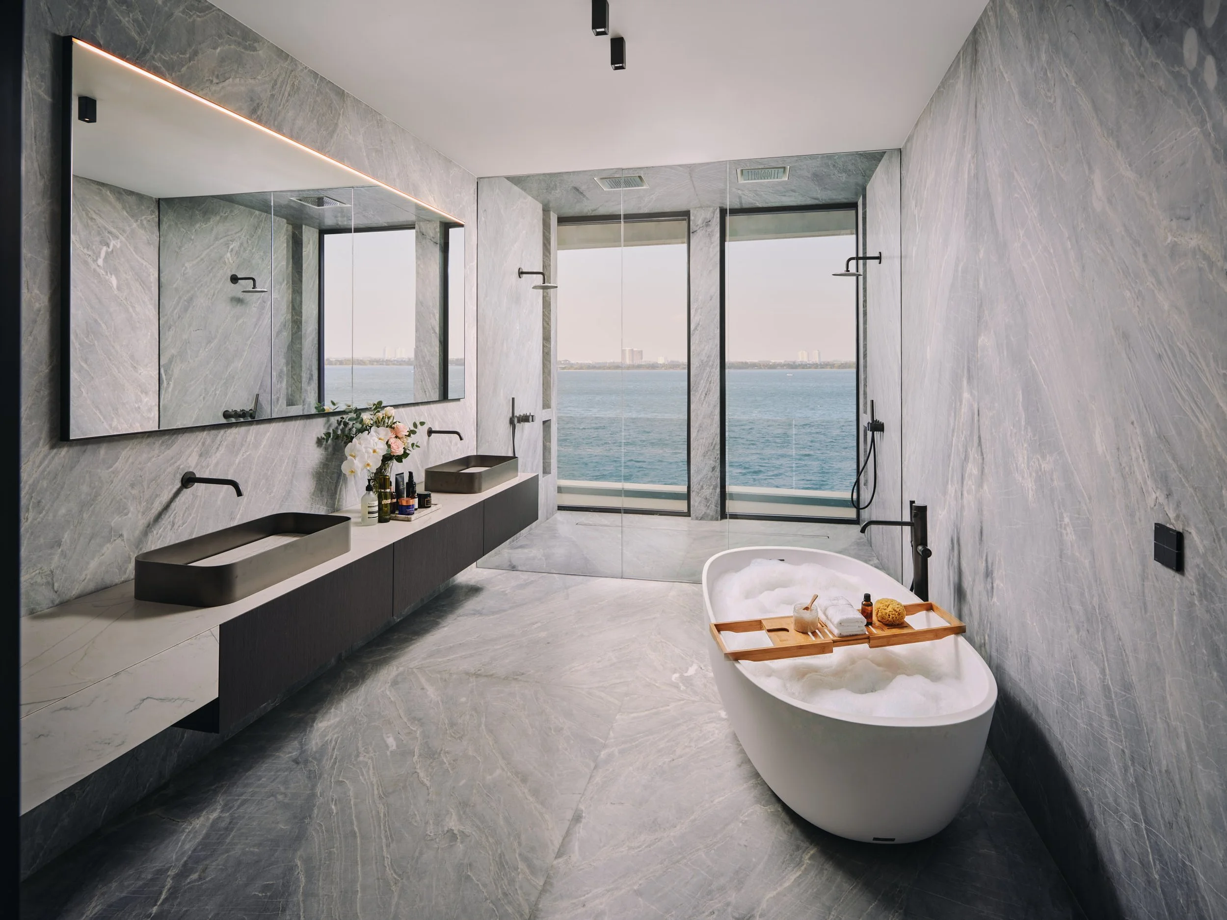 Architectural photograph of a luxury marble master bathroom with freestanding tub overlooking Biscayne Bay in a Venetian Islands waterfront residence in Miami. Captured by Miami and Los Angeles-based architectural photographer Christian Santiago.