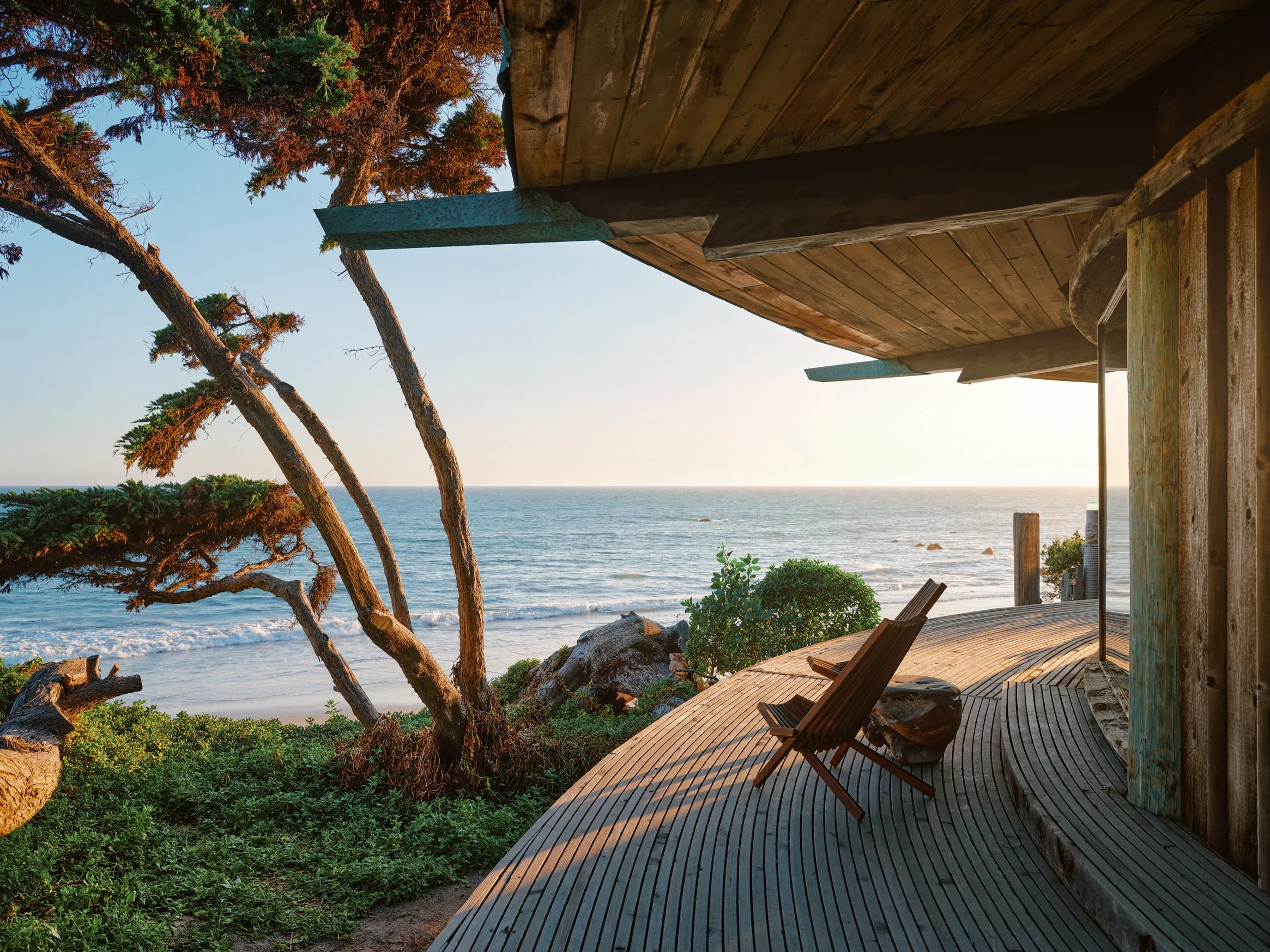 Architectural photograph of the oceanfront deck at the Sandcastle House in Malibu, designed by Harry Gesner. The curving wooden walkway, built from reclaimed telephone poles, leads to a weathered lounge chair overlooking the Pacific Ocean. Cantilever