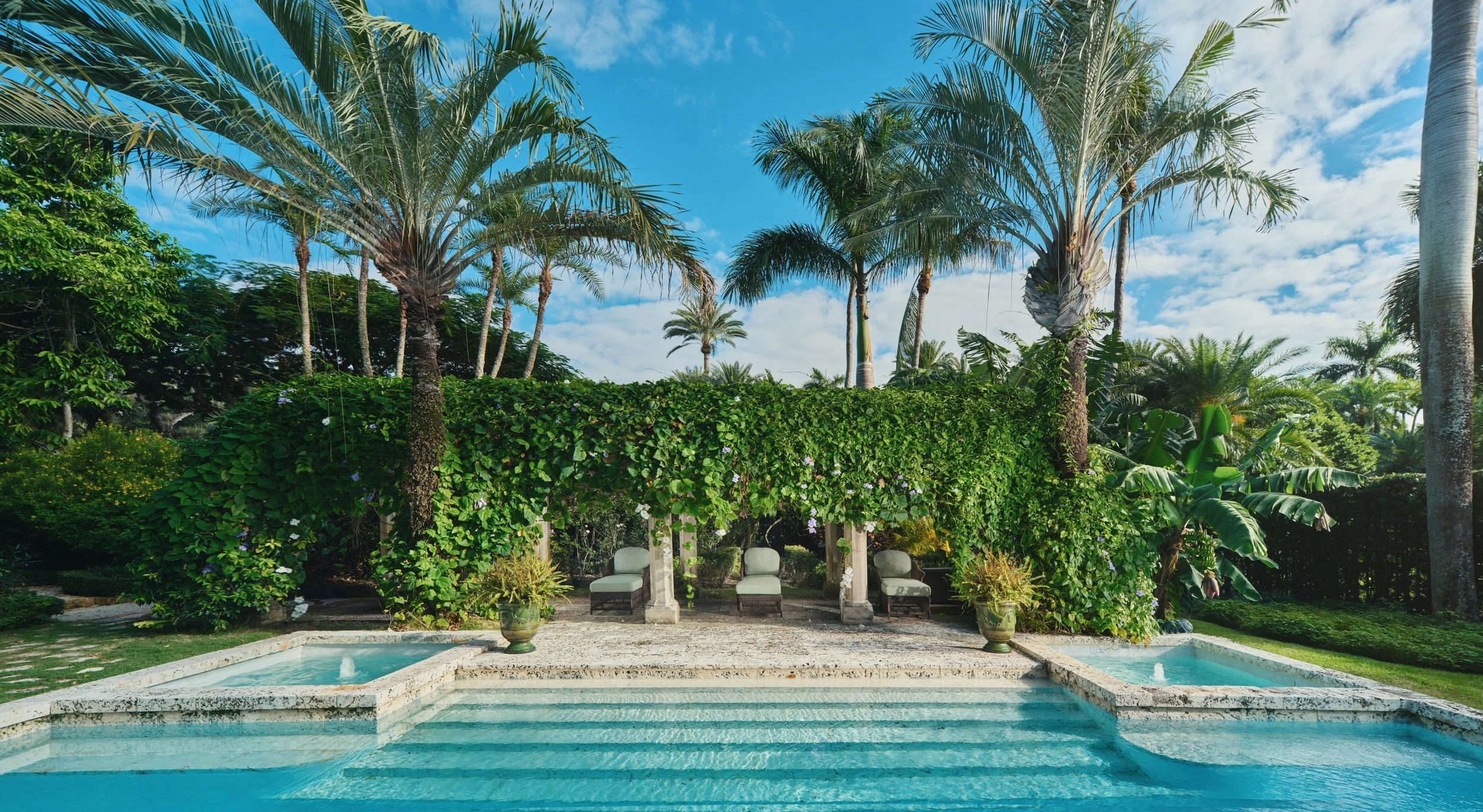 Architectural photograph of a vibrant, arch-shaped hedge framing some loungers in front of a pool in a Mediterranean Revival style villa. Captured by Miami & Los Angeles-based Architectural & Travel photographer Christian Santiago.