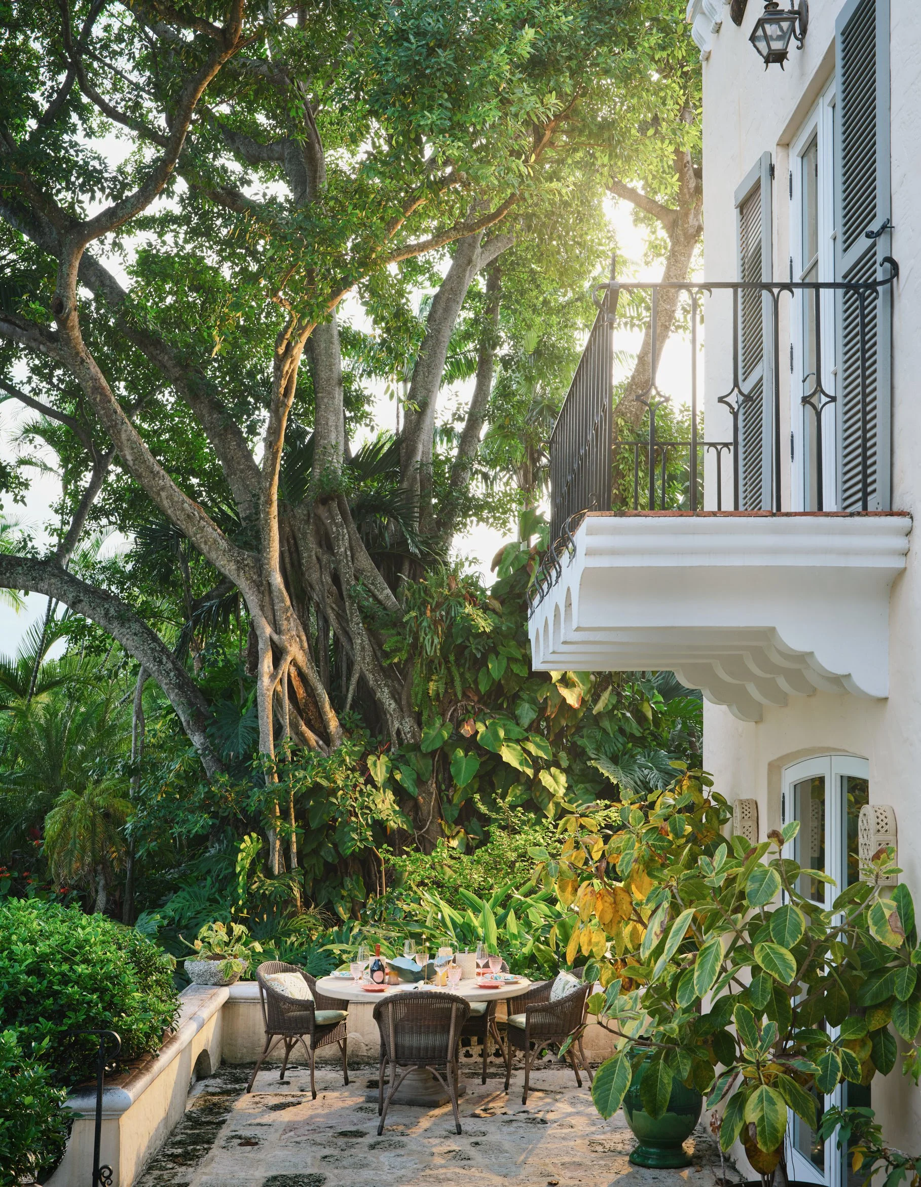 Architectural photograph of Villa Serenita’s shaded outdoor dining terrace nestled beneath a large banyan tree, surrounded by tropical landscaping. Mediterranean Revival estate in Coconut Grove, Miami. Captured by Miami and Los Angeles-based architec