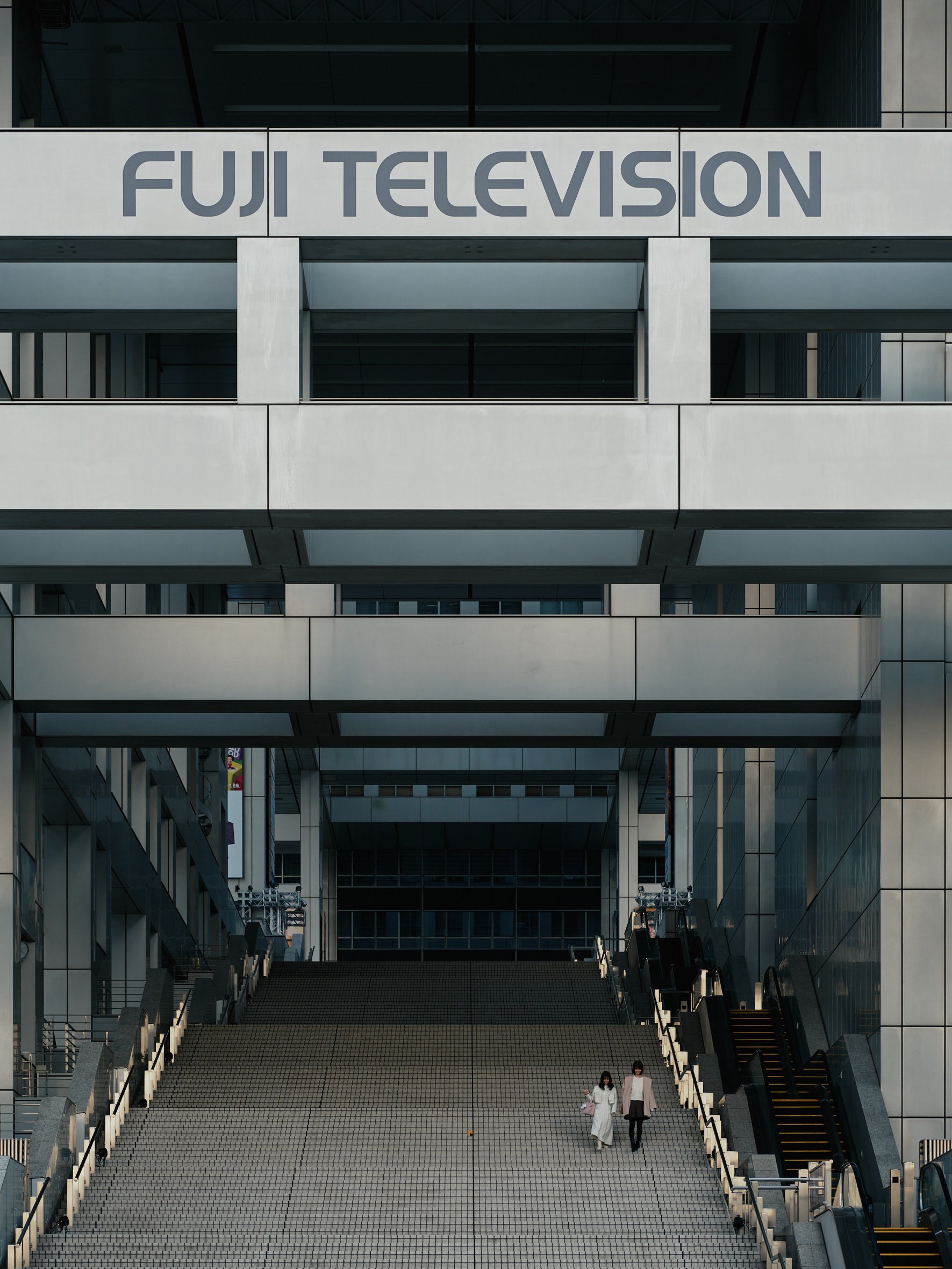 Massive concrete steps lead into the heart of the Fuji TV headquarters, as two figures in white climb toward the monolithic entrance beneath the broadcast tower. Photographed by Miami & Los Angeles-based architectural photographer Christian Santiago