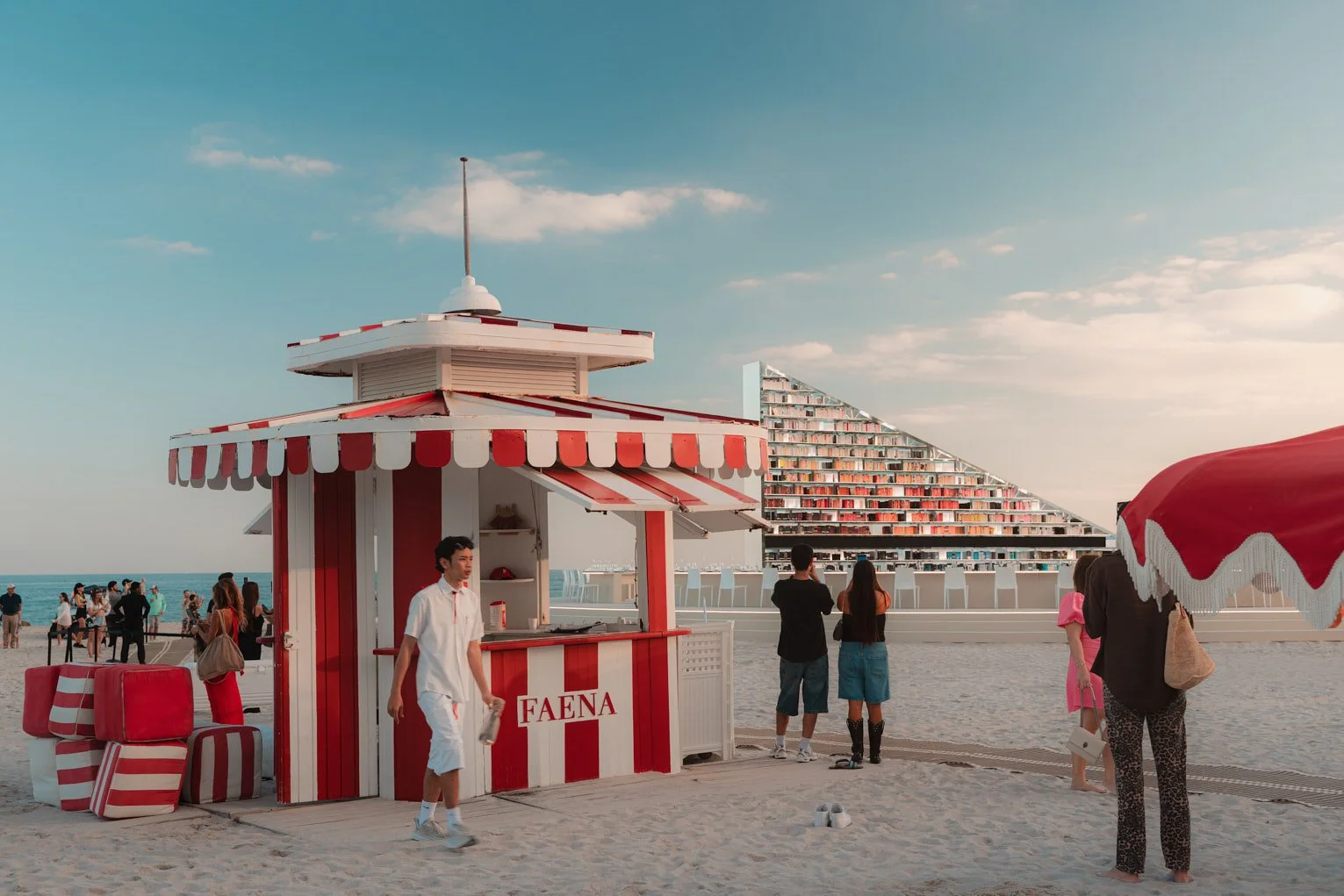 Architectural photograph of Es Devlin’s Library of Us public art installation at Faena Miami Beach during Art Basel Miami Beach, featuring the illuminated triangular bookshelf structure in the background framed by a red-and-white Faena lifeguard stan