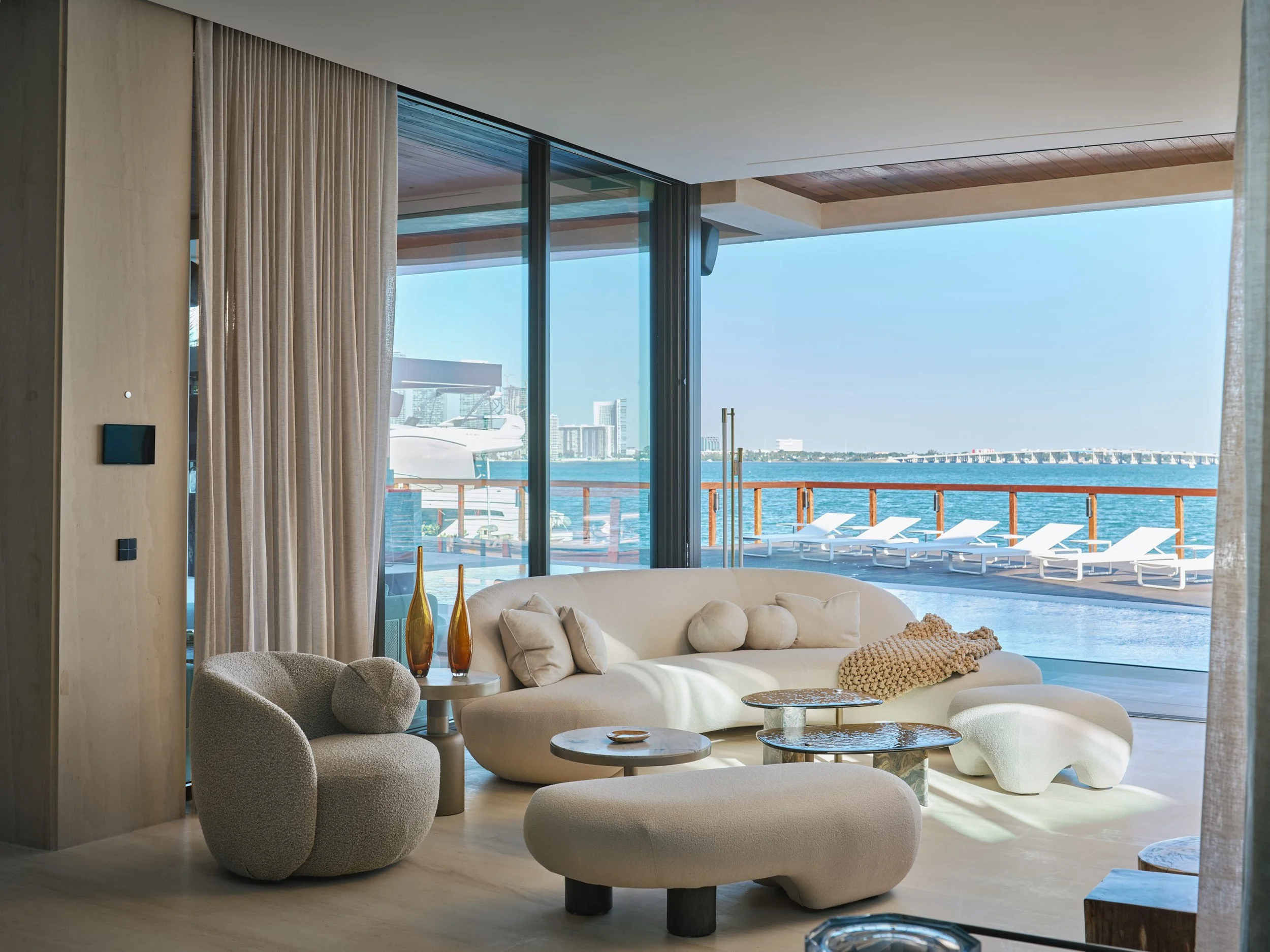 Architectural photograph of a modern waterfront living room with sculptural furniture and floor-to-ceiling glass overlooking Biscayne Bay in a luxury Miami residence. Captured by Miami and Los Angeles-based architectural and travel photographer Chris