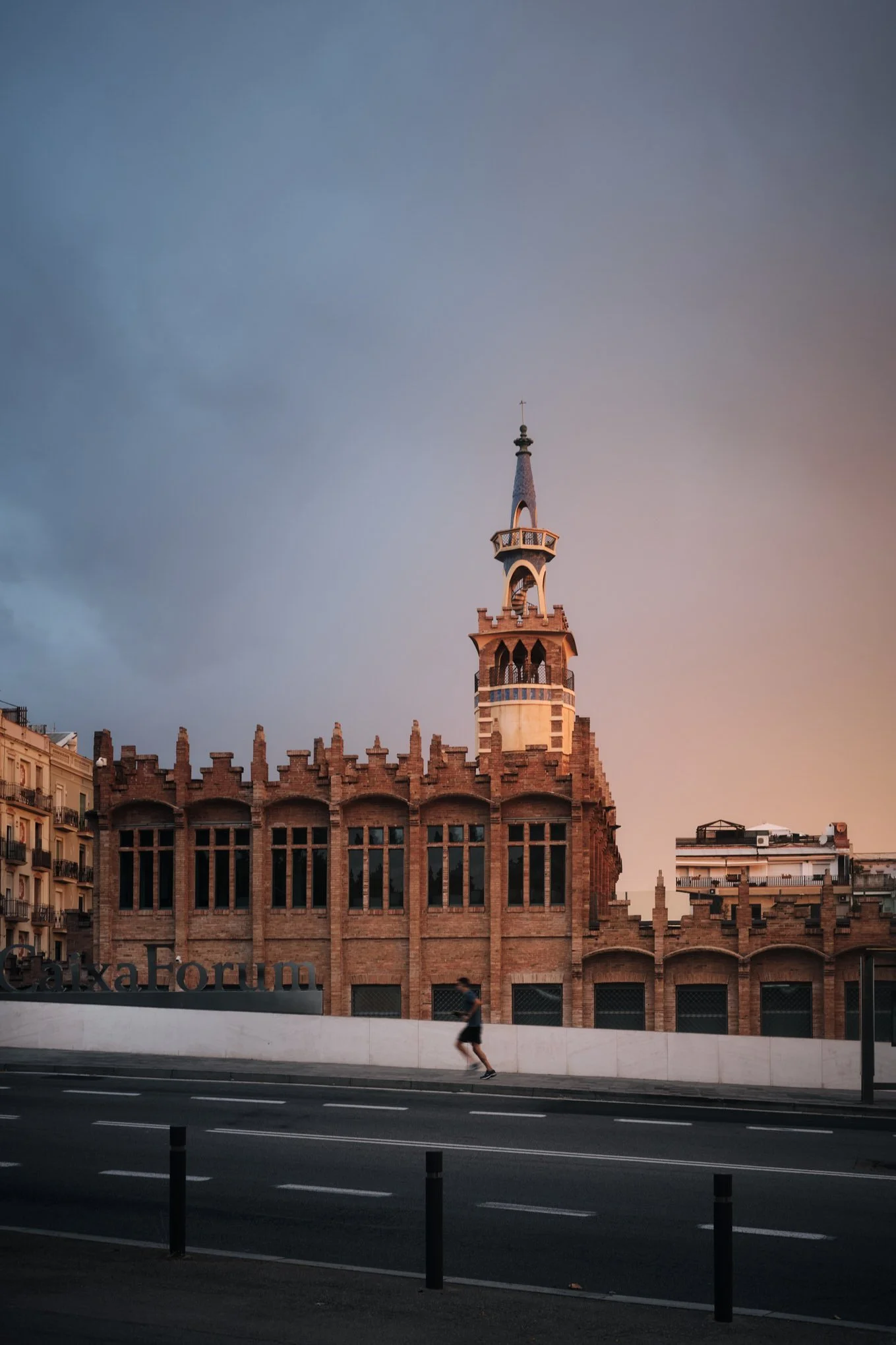Architectural photograph of the CaixaForum cultural center in Barcelona, Spain, captured at dusk with warm light grazing the historic brick façade and ornate tower. This former textile factory, designed in the Catalan Modernisme style by architect Jo