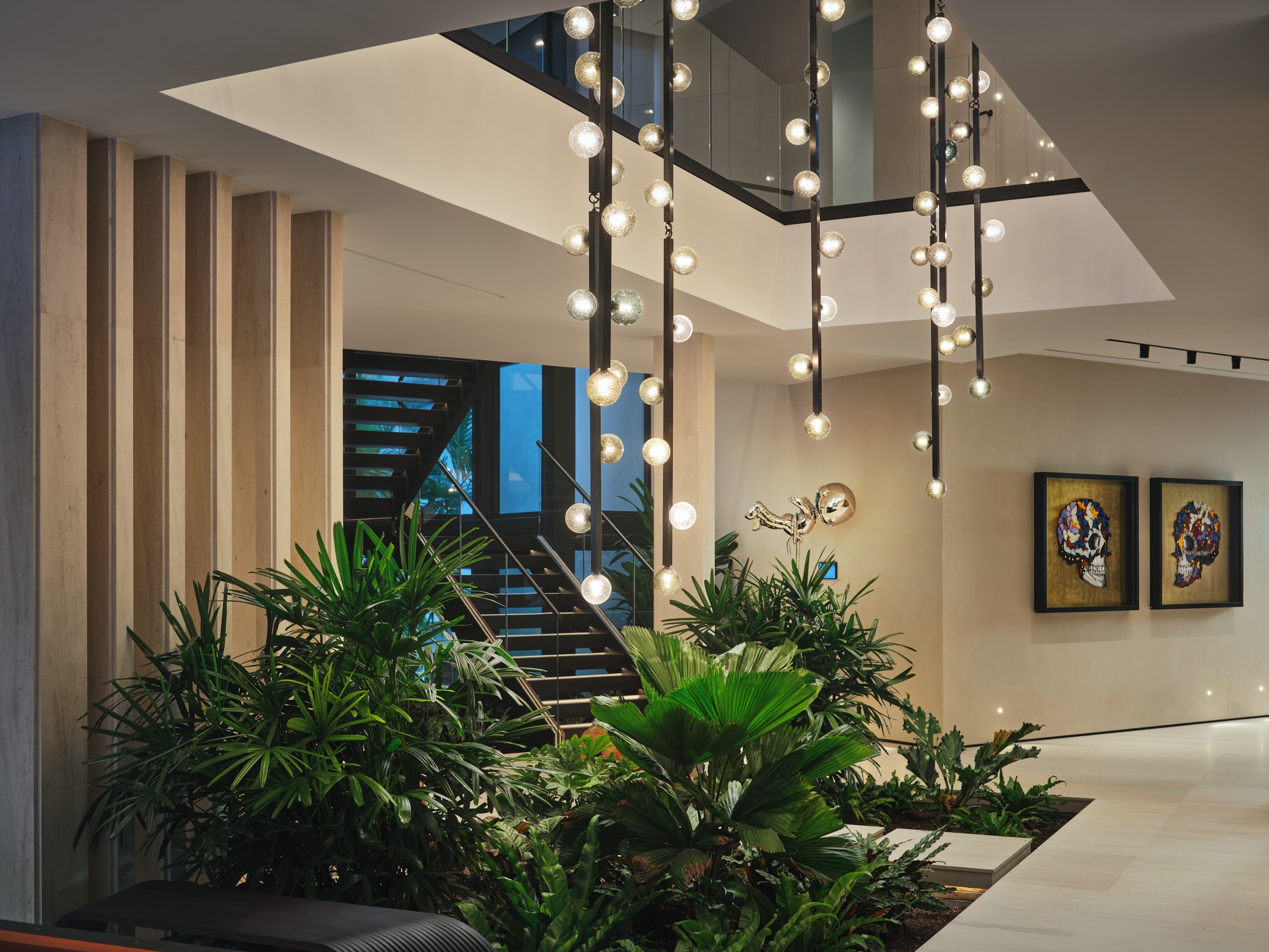 Architectural photograph of a modern residential atrium with sculptural globe chandelier, indoor tropical garden, and floating staircase in a luxury Miami home. Captured by Miami and Los Angeles-based architectural and travel photographer Christian S
