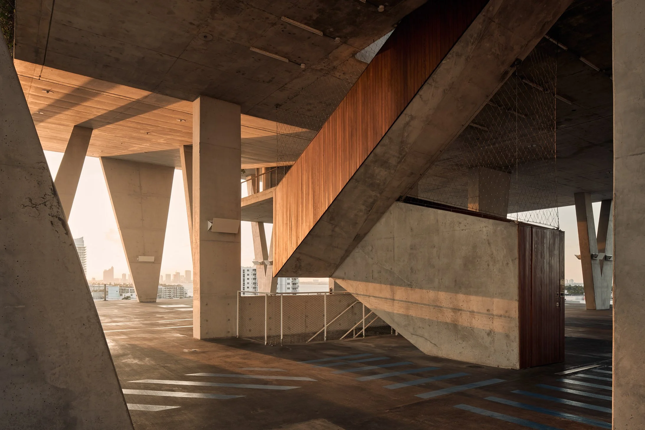 Architectural photograph of 1111 Lincoln Road parking garage in Miami Beach, designed by Herzog & de Meuron. The angular concrete forms, sharp shadows, and exposed staircases are bathed in late afternoon light. This elevated structure doubles as even