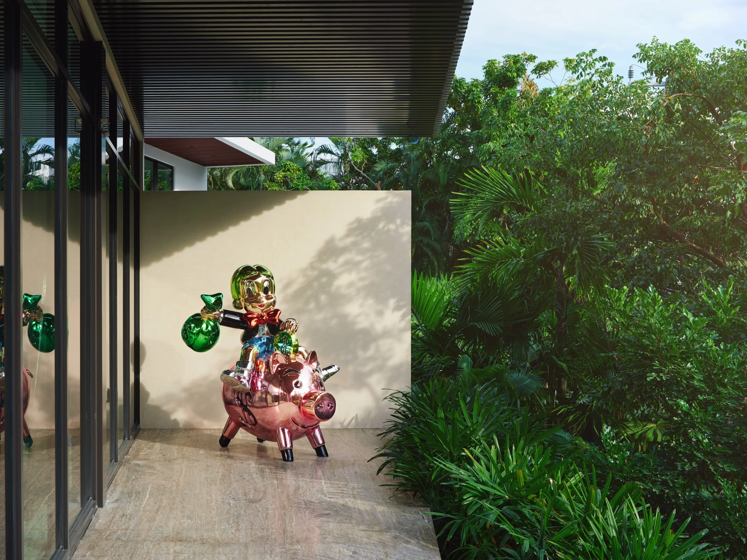 Architectural photograph of a colorful Richie Rich sculpture on a terrace surrounded by tropical landscaping in a Venetian Islands waterfront residence in Miami. Captured by Miami and Los Angeles-based architectural photographer Christian Santiago