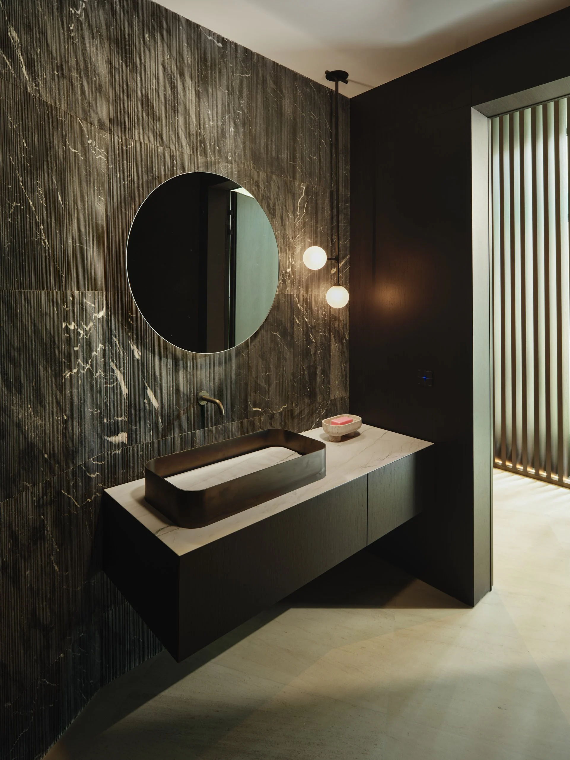 Architectural photograph of a luxury modern bathroom with dark marble wall, floating vanity, and circular mirror inside a Venetian Islands residence in Miami. Captured by Miami and Los Angeles-based architectural and travel photographer Christian San