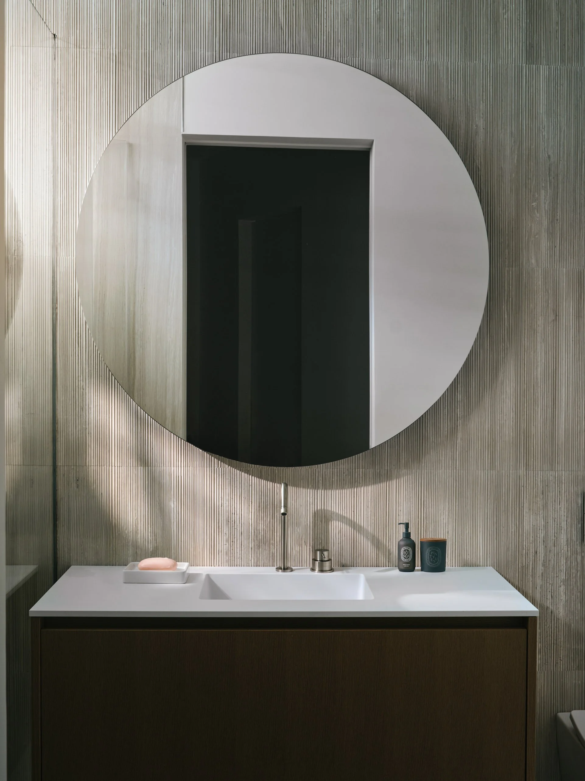 Architectural photograph of a minimalist luxury bathroom featuring a circular mirror, integrated sink, and textured stone wall detail inside a Venetian Islands waterfront residence in Miami. Captured by Miami and Los Angeles-based architectural and t