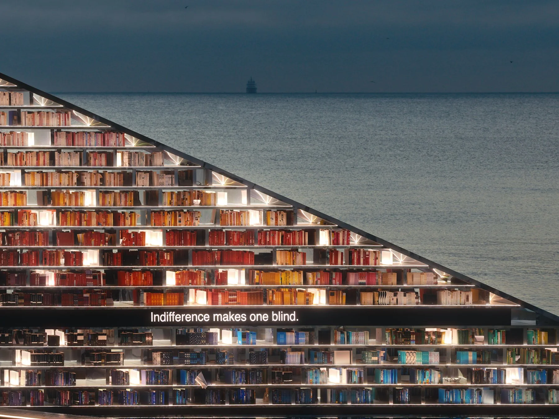 Architectural photograph of Es Devlin’s Library of Us public art installation at Faena Miami Beach during Art Basel Miami Beach, featuring the illuminated triangular bookshelf structure filled with color-coded books and integrated LED text reading “I