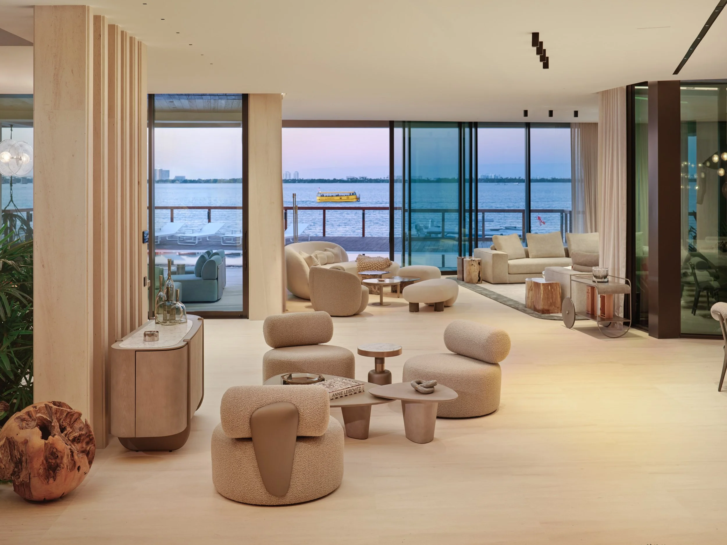 Architectural photograph of a modern waterfront living room at twilight overlooking Biscayne Bay with floor-to-ceiling glass and contemporary furnishings in a Miami luxury residence. Captured by Miami and Los Angeles-based architectural and travel ph