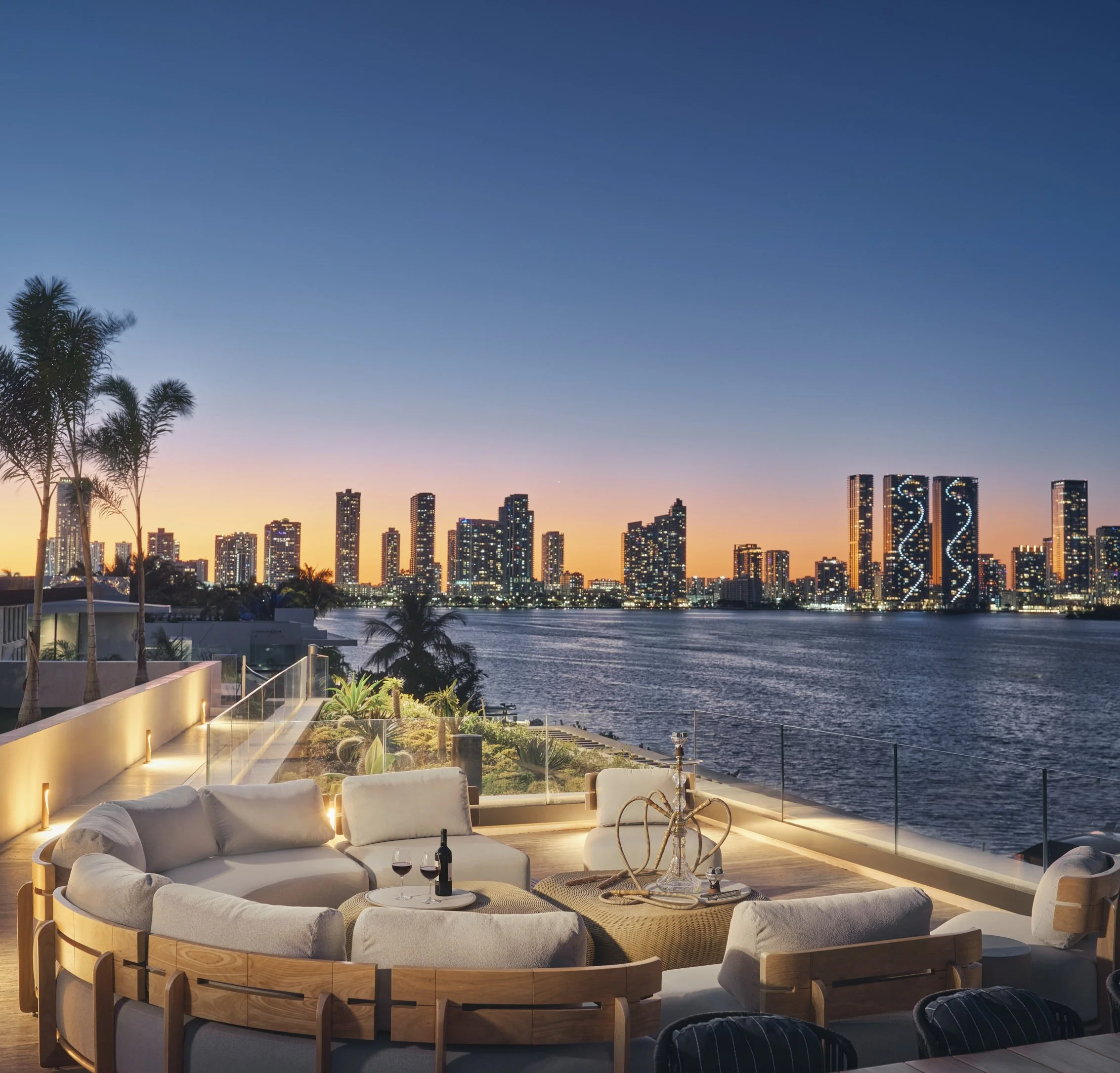 Architectural photograph of a waterfront rooftop terrace at dusk overlooking Biscayne Bay and the illuminated Miami skyline from a Venetian Islands residence. Captured by Miami and Los Angeles-based architectural and travel photographer Christian San