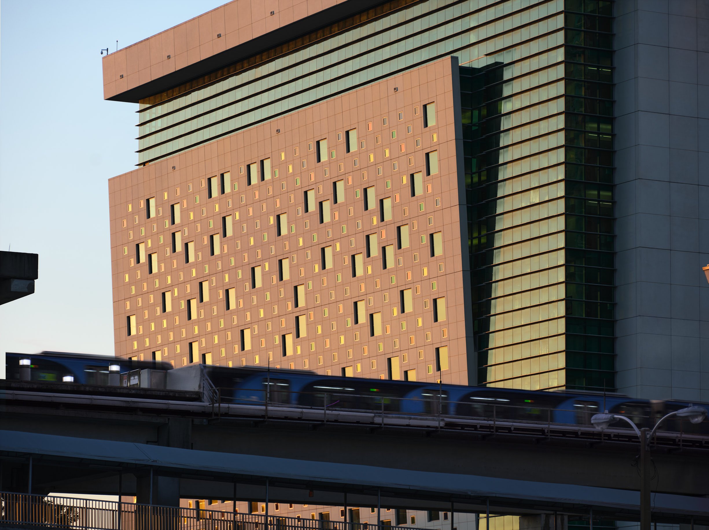 An architectural photograph of the Miami-Dade County Children's Courthouse by HOK Architects. Shot at sunset with a train passing in the foreground. Photographed by Miami & Los Angeles-based architectural photographer Christian Santiago.