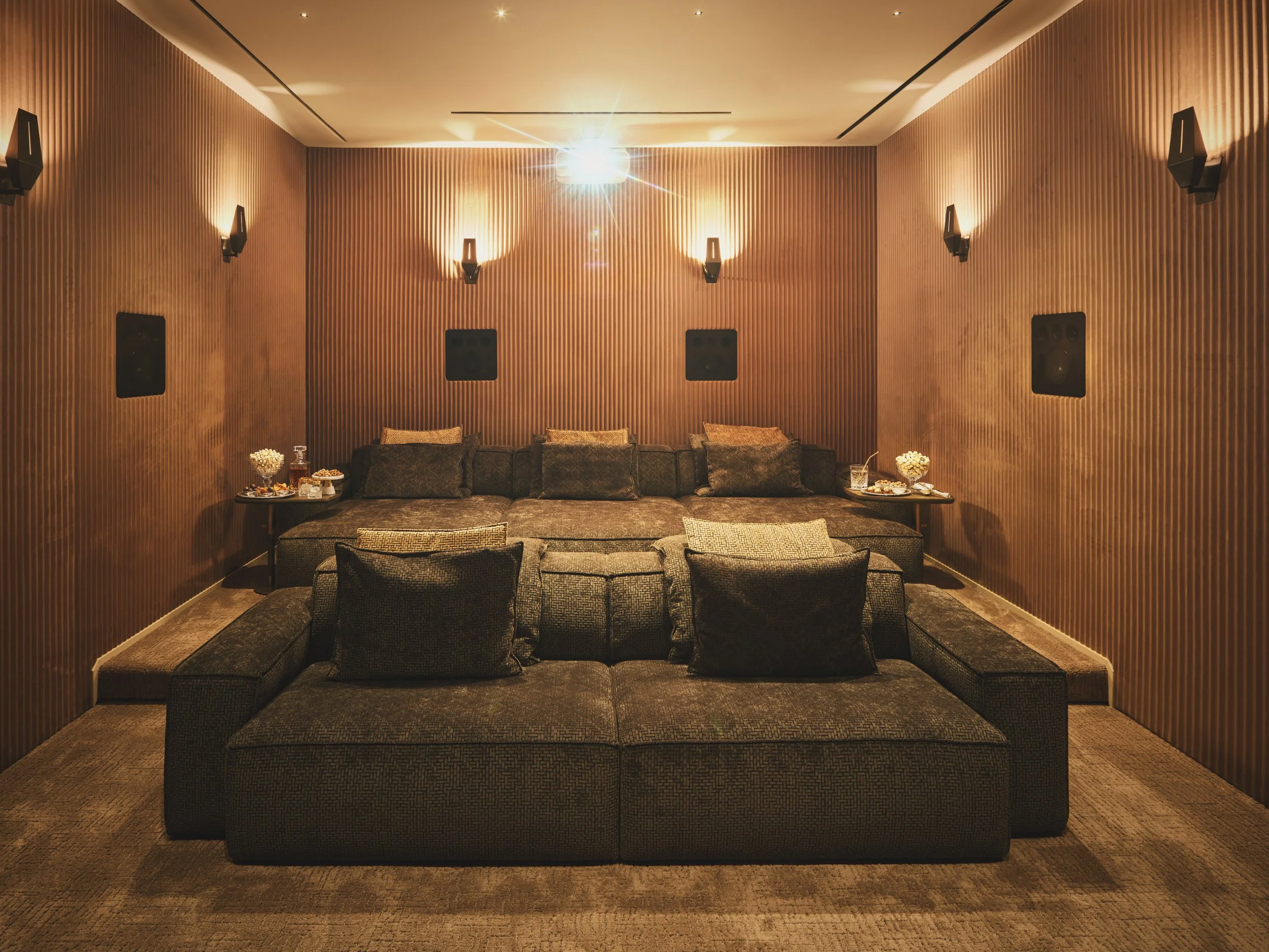 Architectural photograph of a luxury home theater featuring layered sectional seating, integrated surround sound speakers, and warm wood acoustic panel walls inside a modern Miami residence. Captured by Miami and Los Angeles-based architectural and t