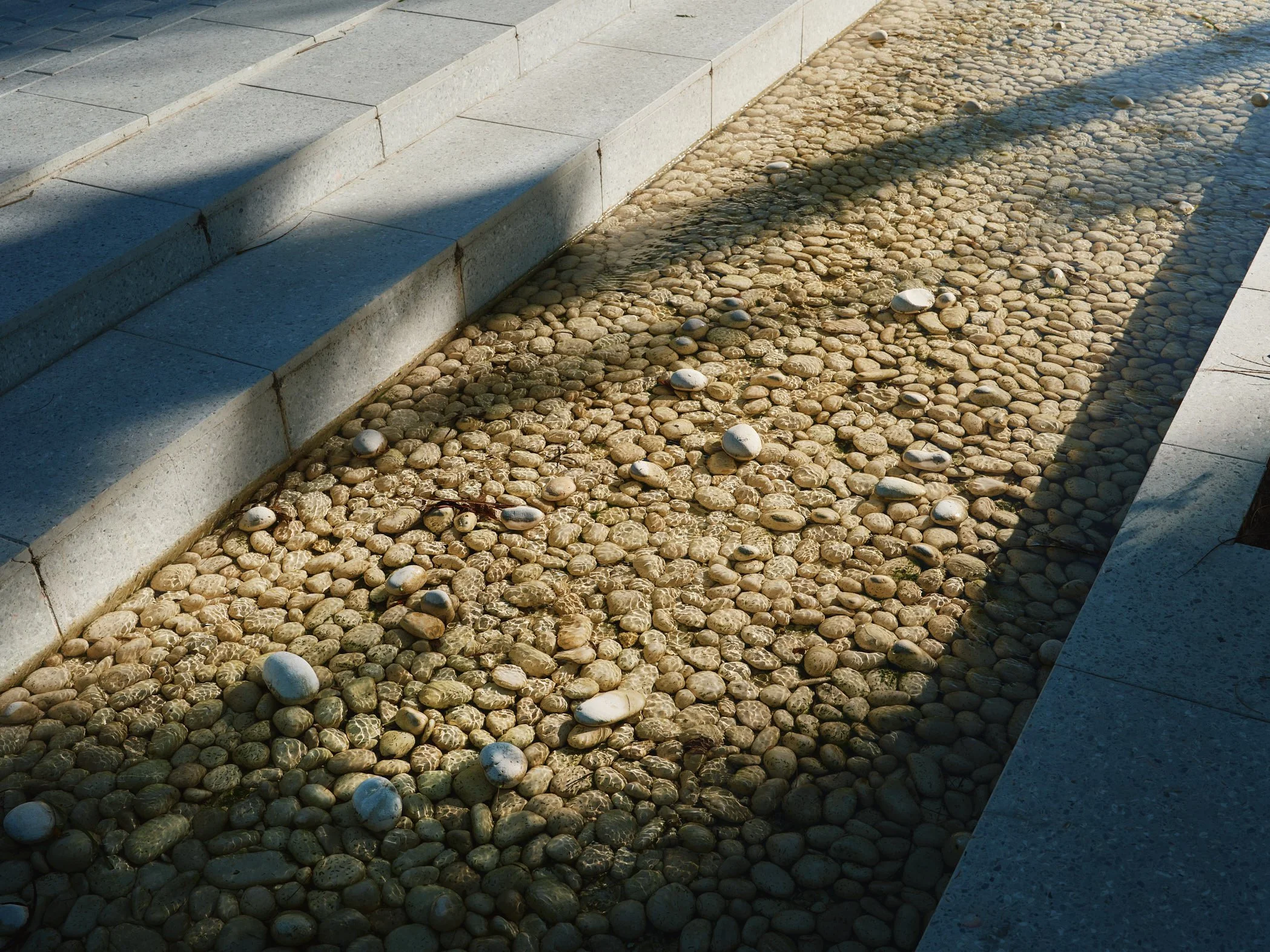 Architectural detail photograph of the stone-lined water feature and stepped concrete terraces at Bayshore Park in Miami Beach, showing the tactile materials and landscape architecture design elements that shape the park’s interactive public spaces. 