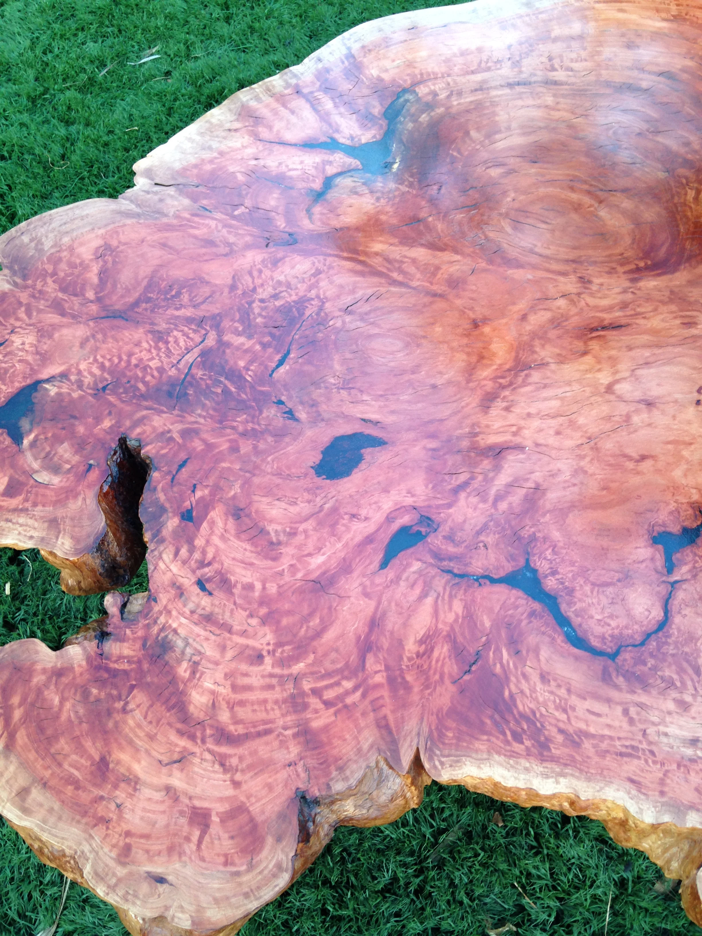 Close-up of a large wooden table with a polished surface, showing natural wood grain and some cracks, placed on a grassy area