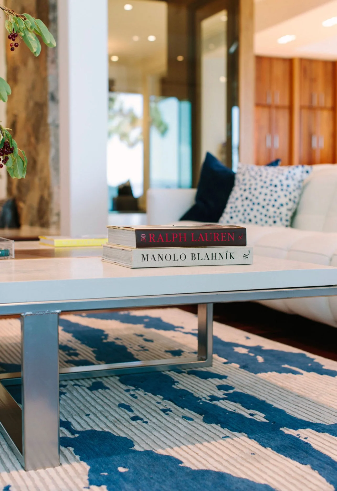 Stack of two books on a coffee table in a modern living room, with a white sofa and patterned pillows in the background.