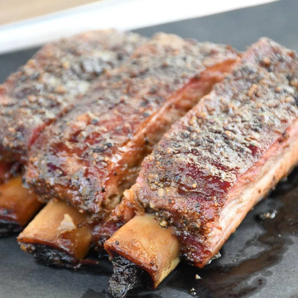 BRETT’S BACKYARD BARBECUE (TEXAS MONTHLY TOP 25 NEW JOINTS) Home: 449 W. Cameron Avenue, Rockdale, Texas Owner & Pitmaster: Brett Boren Serving: Cowboy Pork Steak with Fried Tortilla and Pineapple for VIP Ticket Holders and Sausage, Pork Belly with Peach Bourbon and dessert for General Admission. Brett Boren was bitten by the BBQ bug at an early age, starting with the competition barbecue world. After years of competing in cookoffs and winning multiple awards, Brett began to contemplate a retail business. After building up his profile with a series of successful pop-ups and many large catering jobs, Brett found a location in the small town of Rockdale, Texas that would allow him to put down roots. Brett began the build out of his spot and opened with a bang at the end of October, 2018 serving BBQ staples and specials cooked well on his custom made Moberg pits. — from Tales from the Pits Read More: https://www.texasmonthly.com/bbq/top-25-new-barbecue-joints-texas/