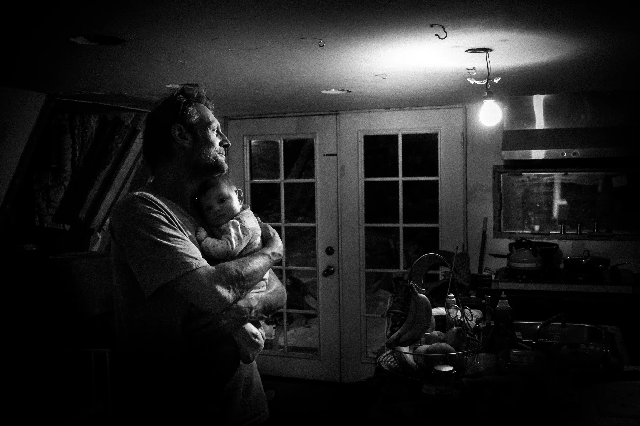 Molly Rees Photo - Black and White Documentary Family Photography - Father and baby portrait in kitchen at night by M. Menschel