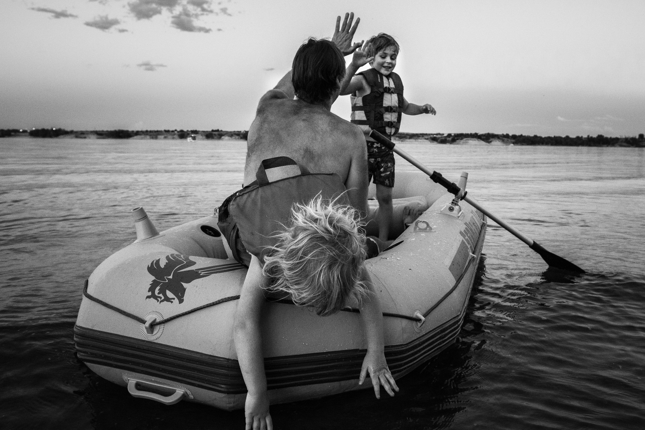 Blog - The Pen & Camera - Molly Rees Photo - Black and White Documentary Childhood Photography - children in raft giving high-five at Chatfield Reservoir in Denver, Colorado by M. Menschel