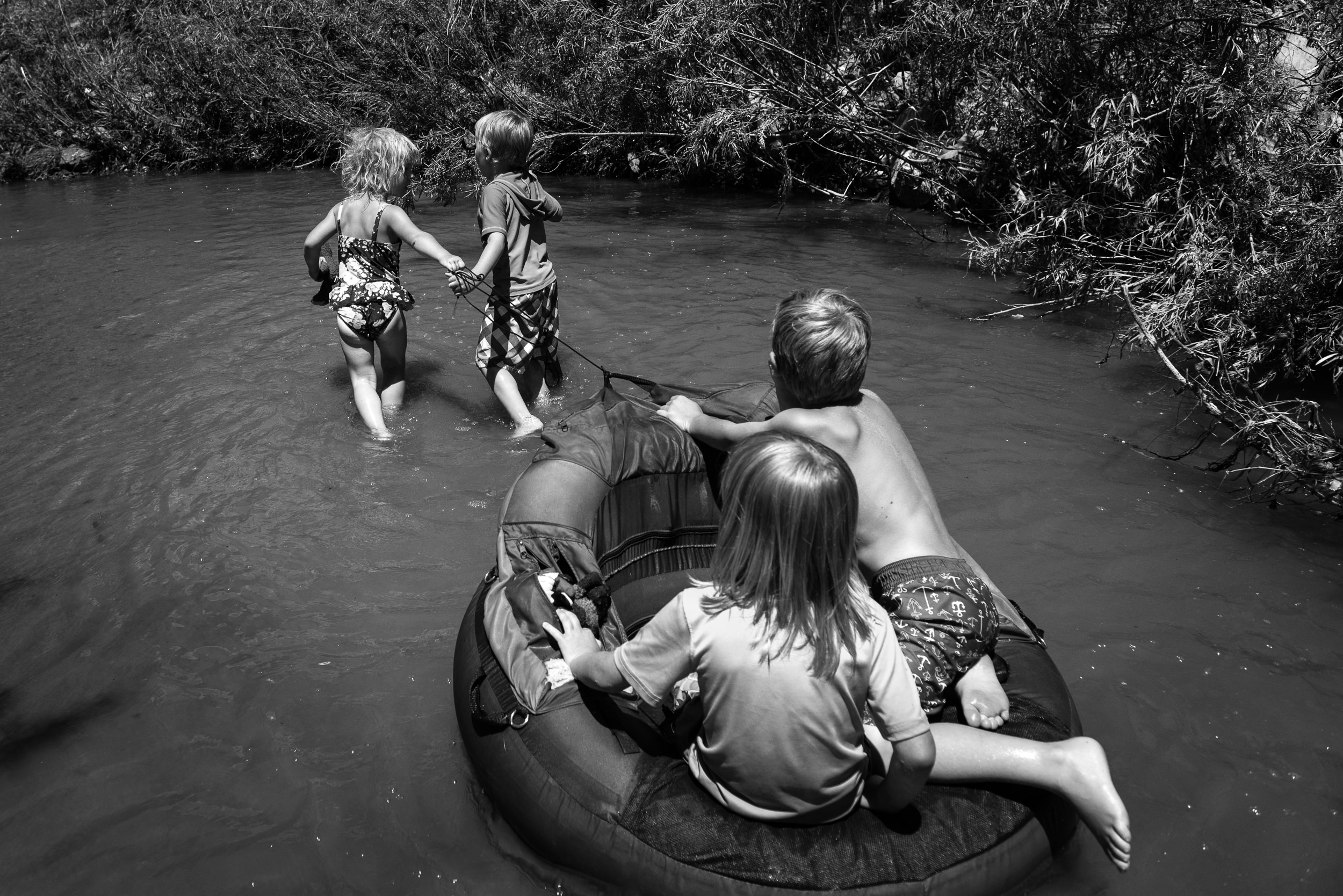 Blog - The Pen & Camera - Molly Rees Photo - Black and White Documentary Childhood Photography - children tubing in stream through woods at Belleview Park in Denver, Colorado by M. Menschel
