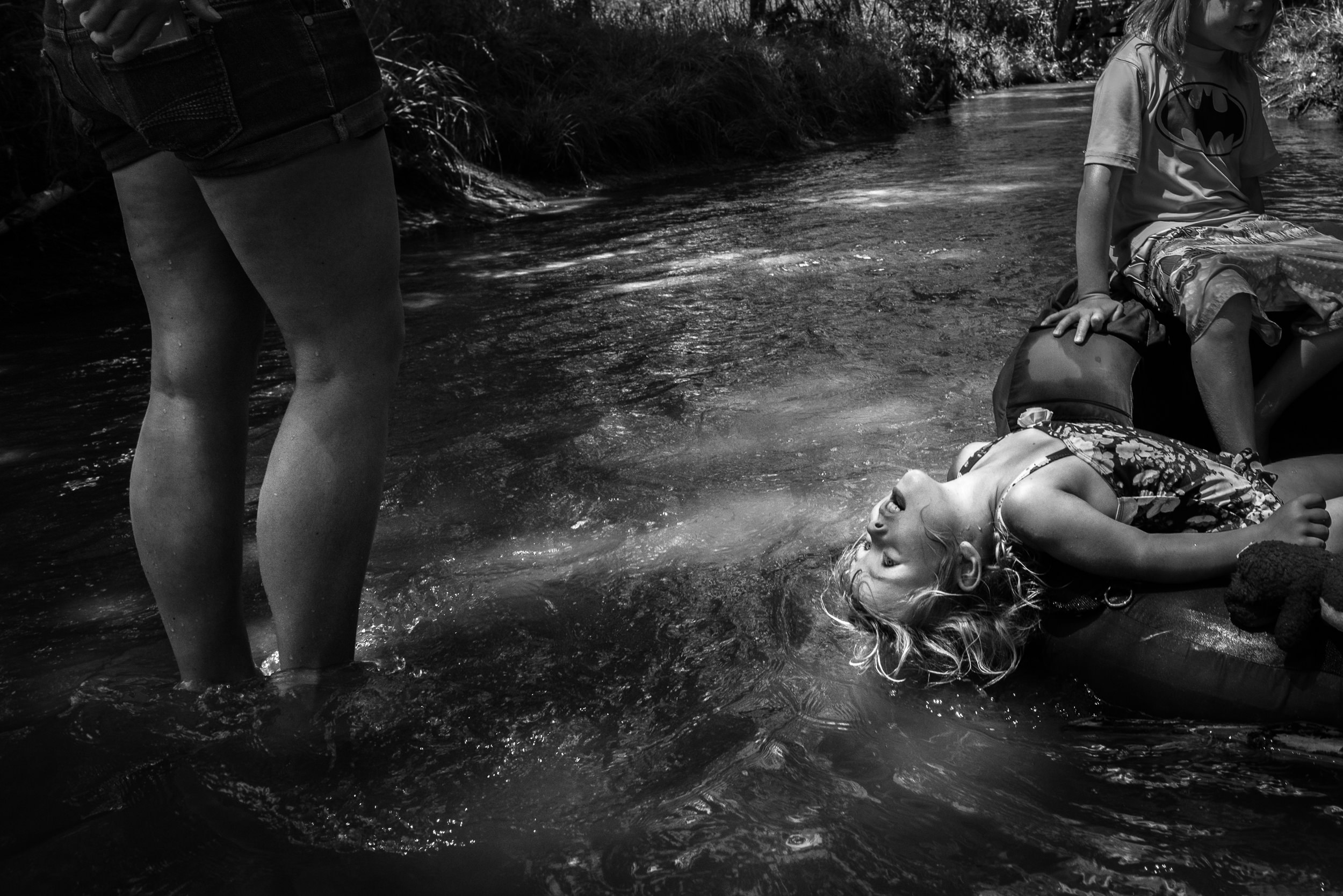 Blog - The Pen & Camera - Molly Rees Photo - Black and White Documentary Childhood Photography - children tubing in stream through woods at Belleview Park in Denver, Colorado by M. Menschel