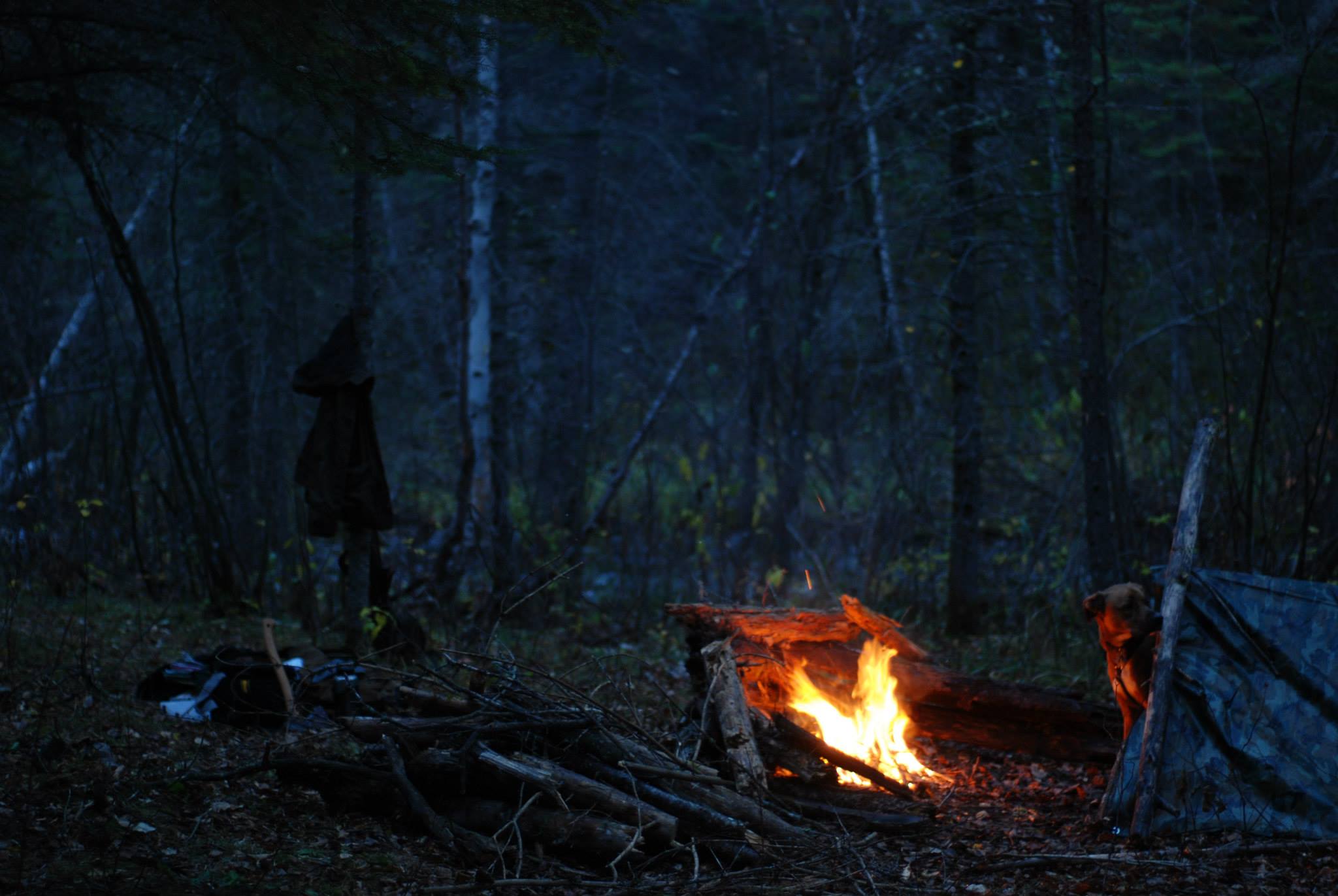 The shelter is up, blanket laid down, and fire roaring. Jean Paul finds his place for the night.