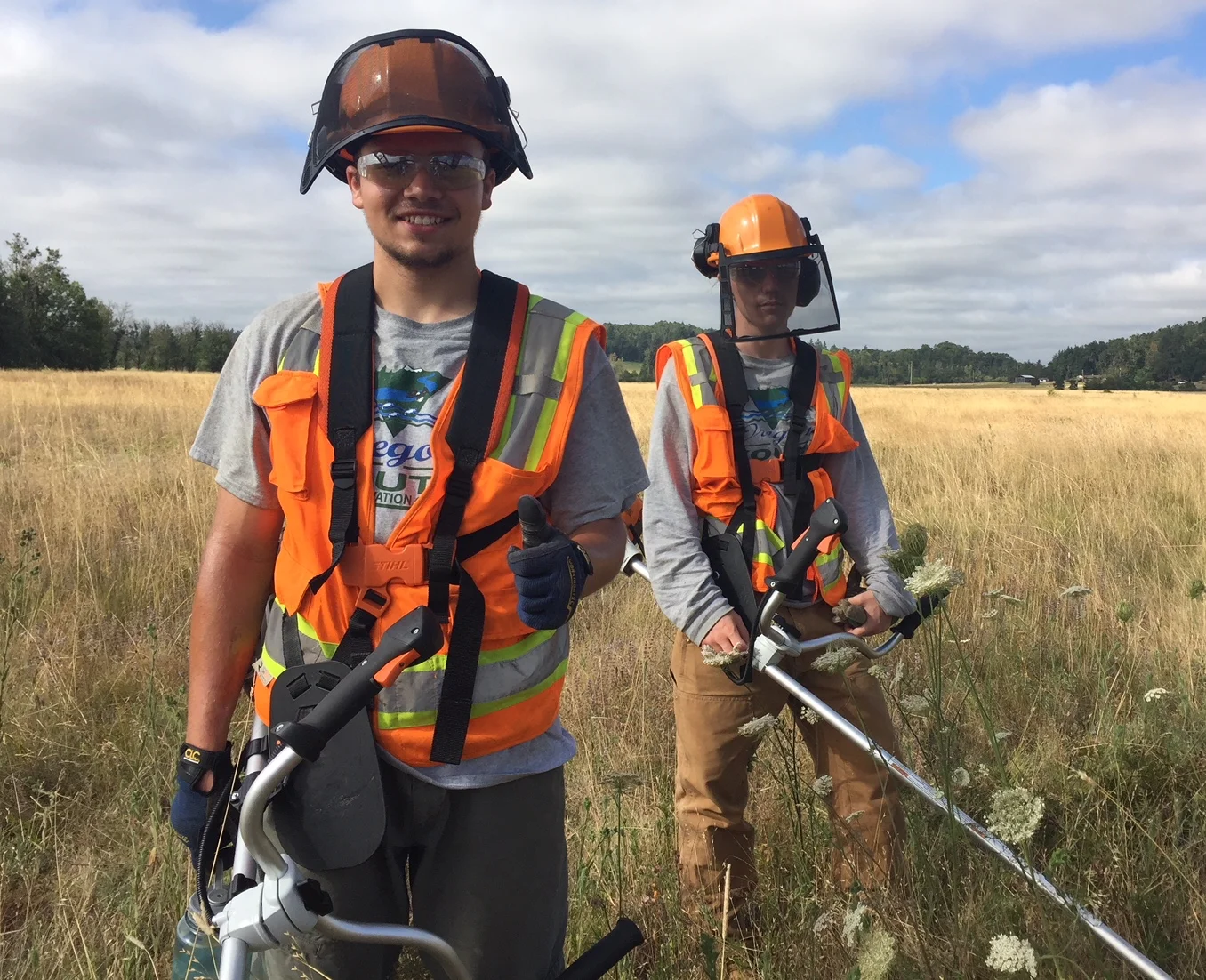 2 members of Looking Glass' Lane Metro Youth Corps summer work crew show off their brush cutters as they trim invasive species from fields in West Eugene.