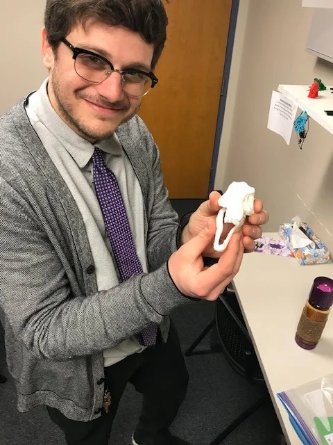 Ethan posing with the skull of a full model dinosaur a student is currently working on printing.