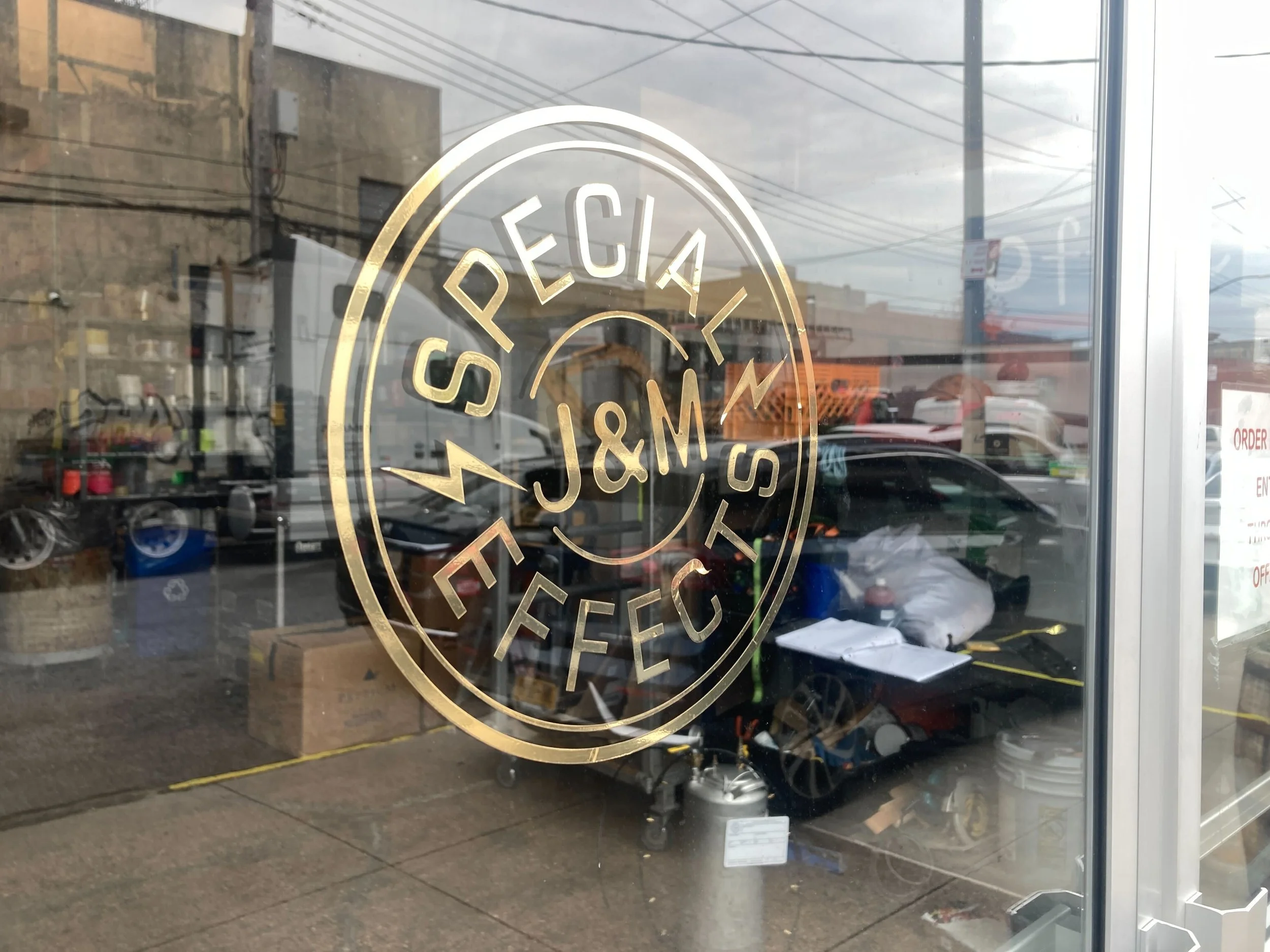 An image of a glass storefront with a golden logo on it, reading "J&M Special Effects)
