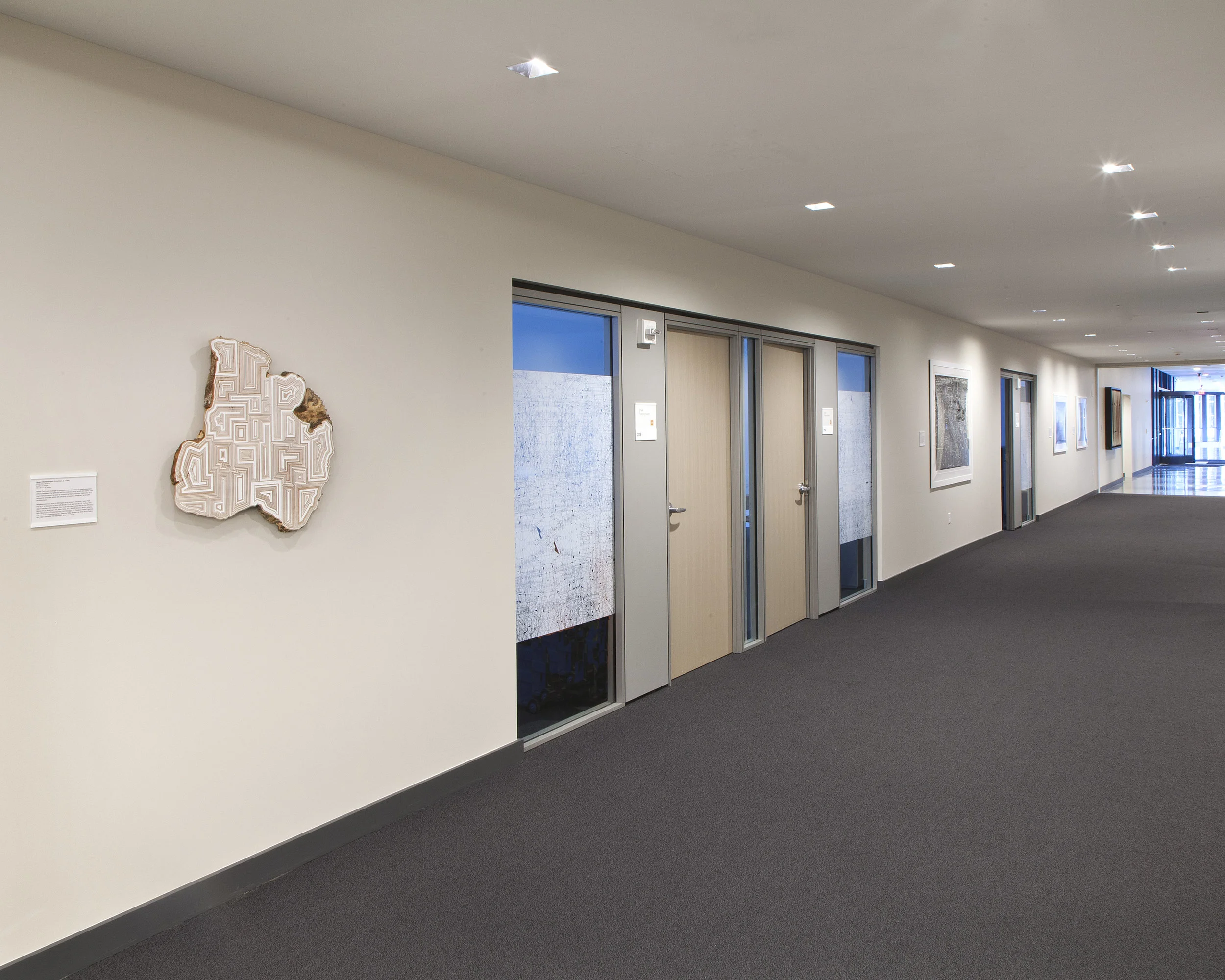 Artworks by Jason Middlebrook, Paula Scher, and Buckminster Fuller are on one side of the hallway leading into the conference center. 