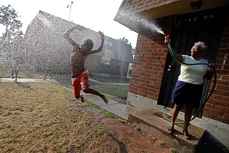 Charlie Lee, of Newark, tries to water her grass, and ends up watering Kasheem Heath, 9, a neighbor, on a hot day in Newark. (Photo Credit: Saed Hindash)