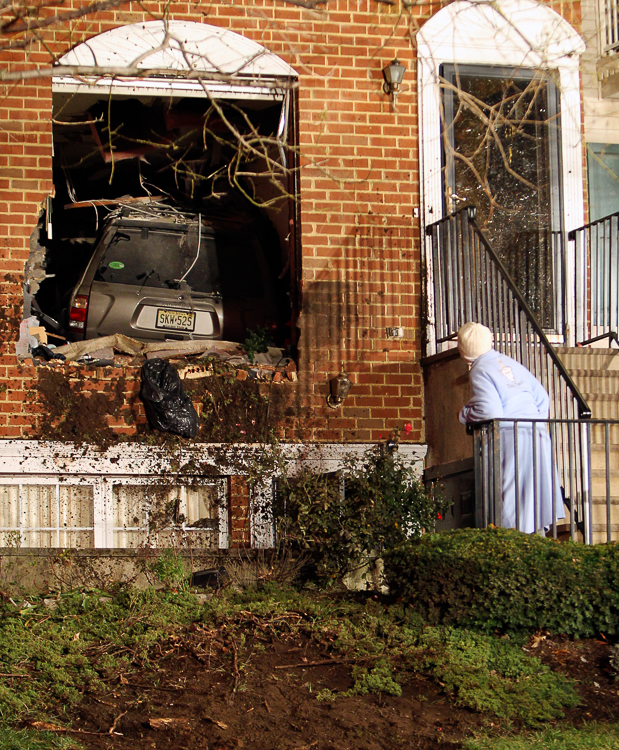 A neighbor takes a peek at a Nissan Pathfinder which crashed and landed in the house belonging to Gloria Sinclair, 74, Friday night December 8, 2011, near the intersection of West Market Street and Wickliffe Street in Newark. No one was injured. (Photo Credit: Saed Hindash)