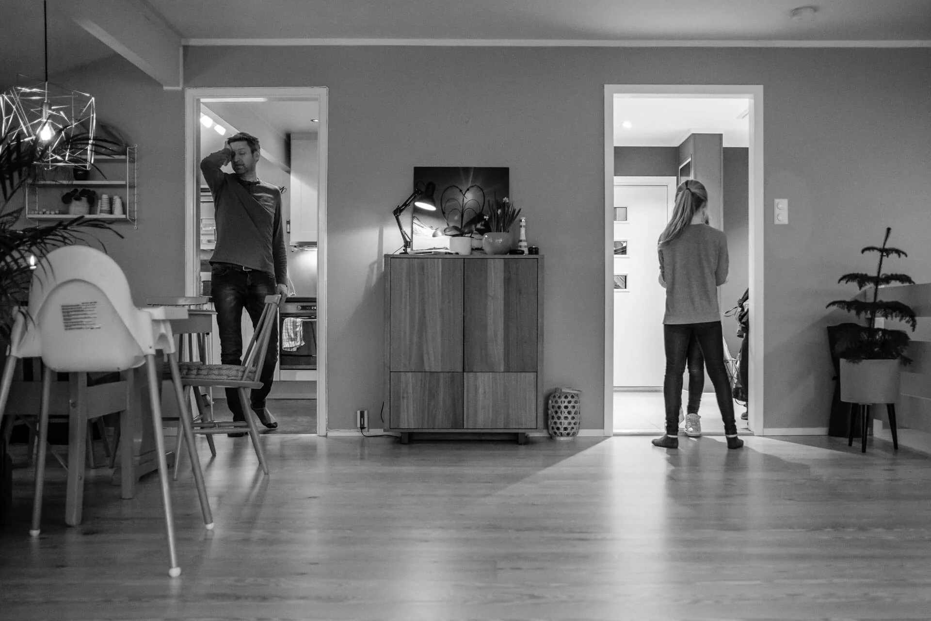I stua hjemme hos barnefamilie. To barn står med ryggen til i en døråpning, far står i en annen døråpning og ser ganske sliten ut. De ser ikke hverandre.