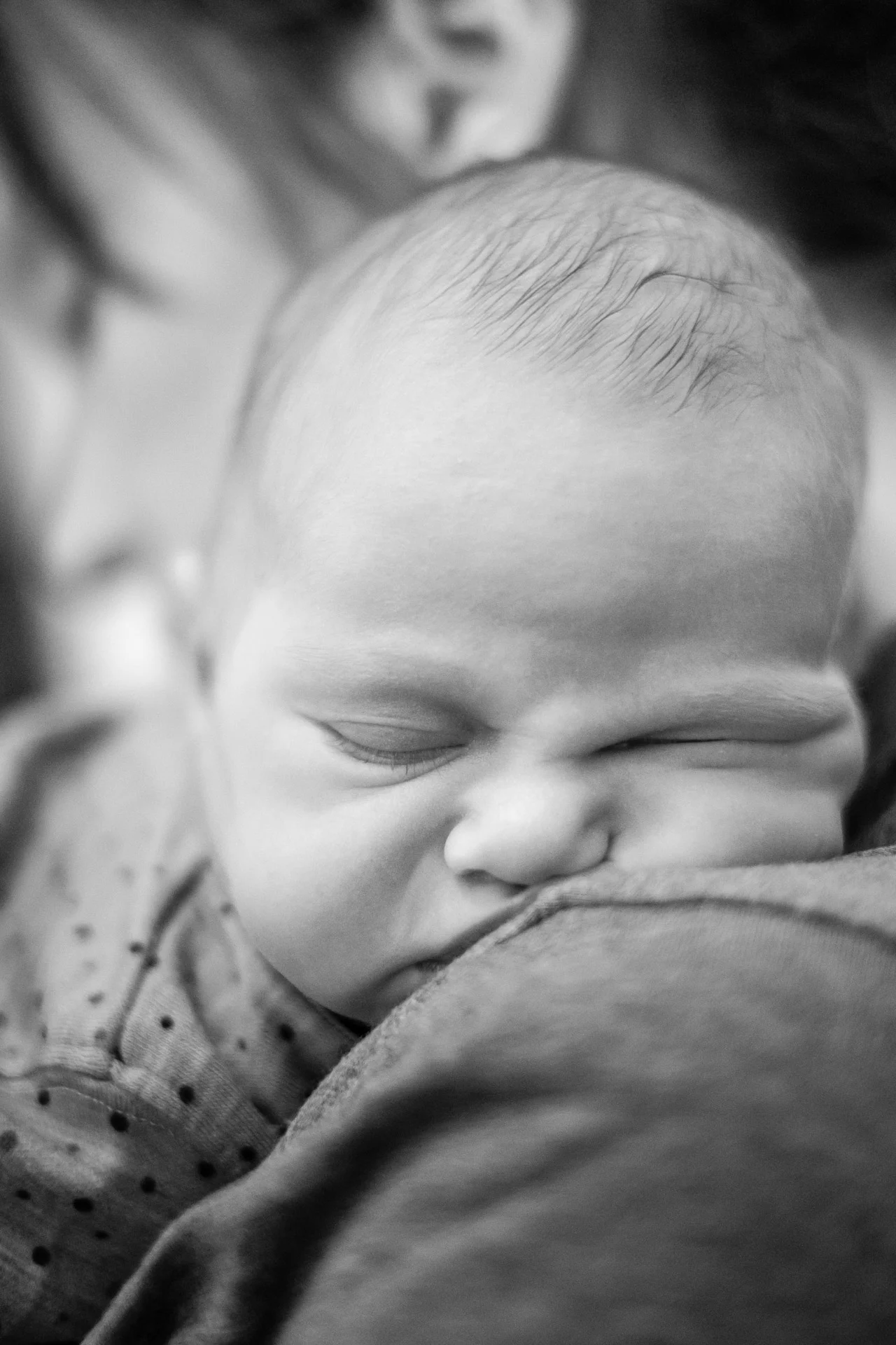 Nyfødt baby ligger på skulderen og sover. Ansiktet er delvis trykket sammen, og det er tydelig at babyen slapper veldig godt av.